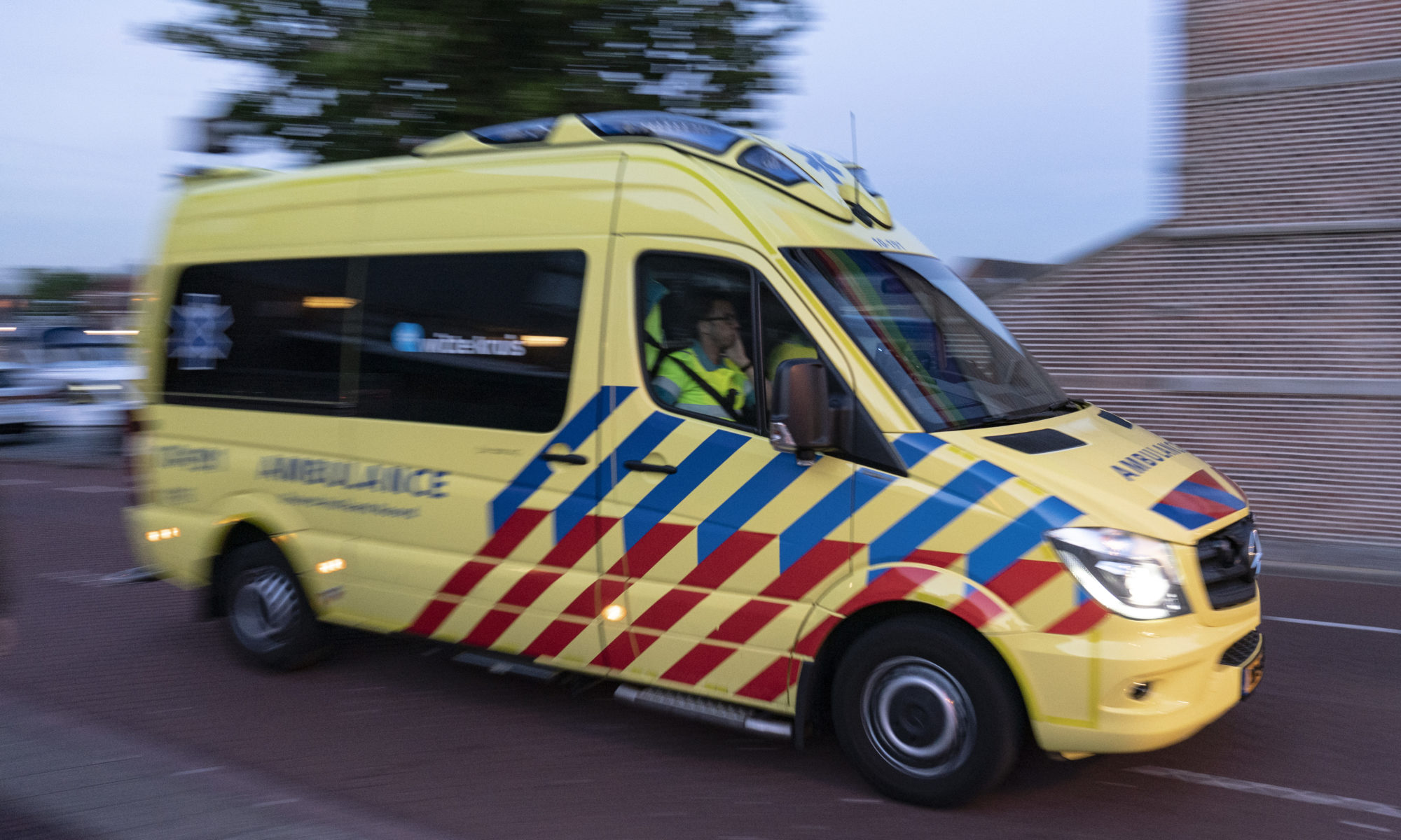 Geel-rode ambulance met zwaailichten aan rijdt over straat.