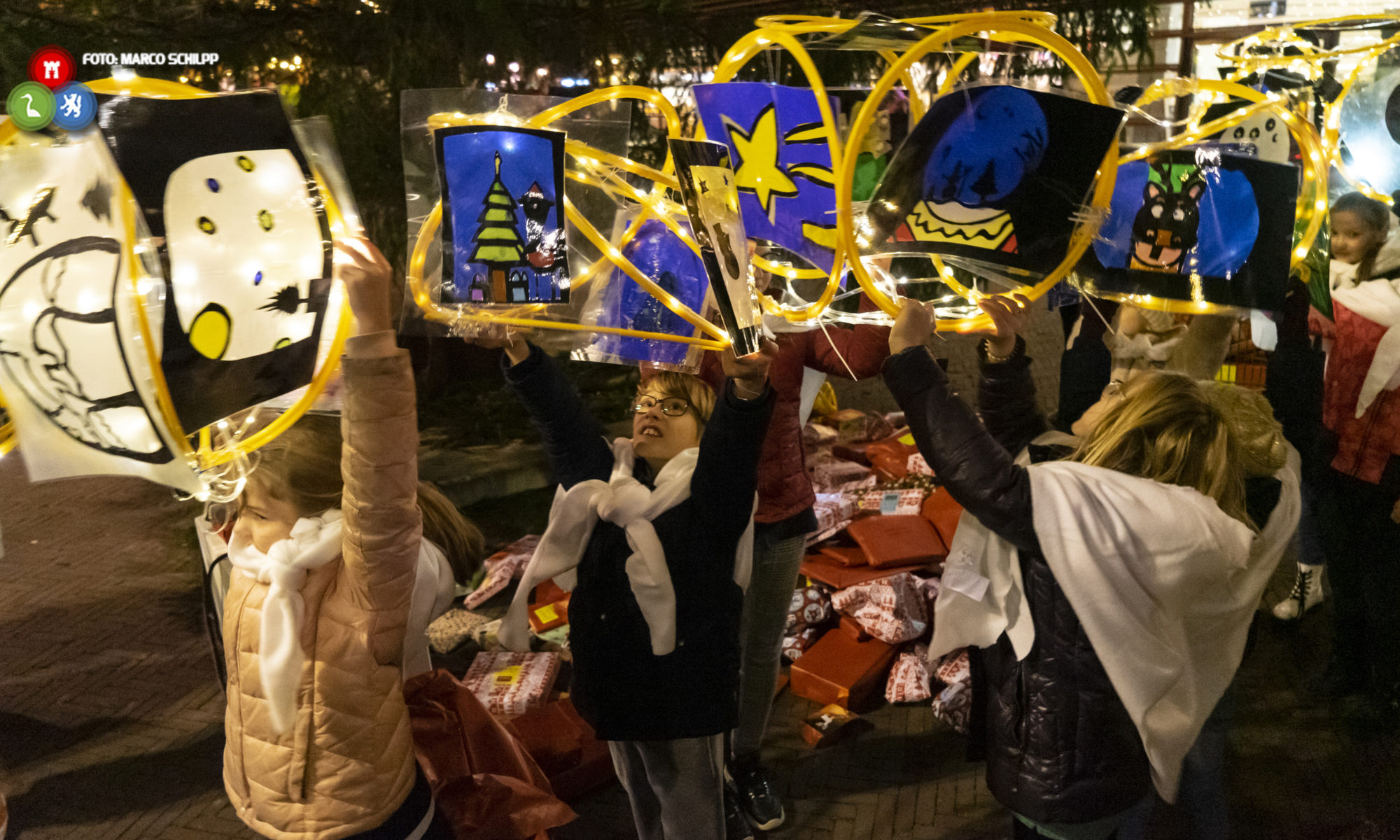 Cadeaus en lichtobjecten neergelegd onder feestelijk ontstoken kaaskerstboom