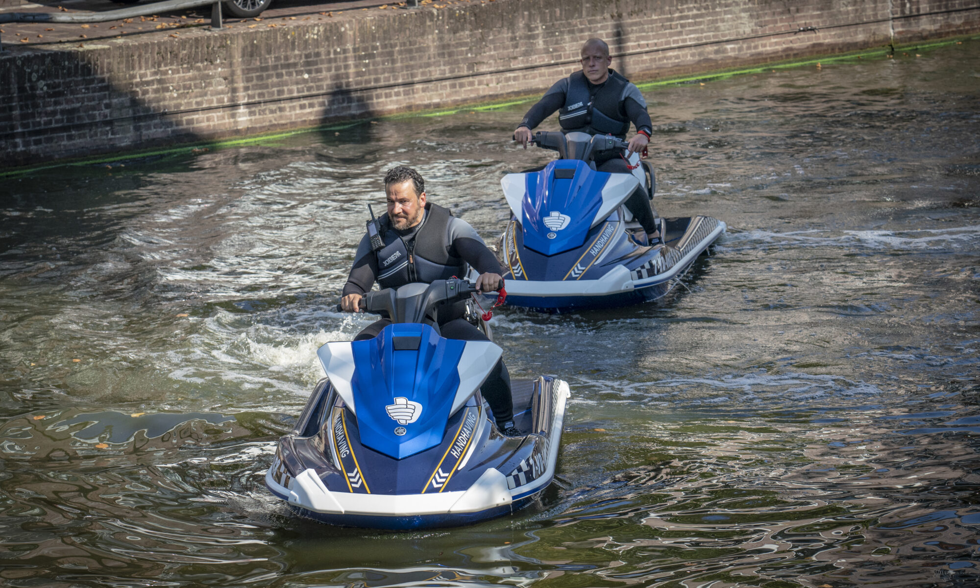 Twee mannen op jetski's in een kanaal.