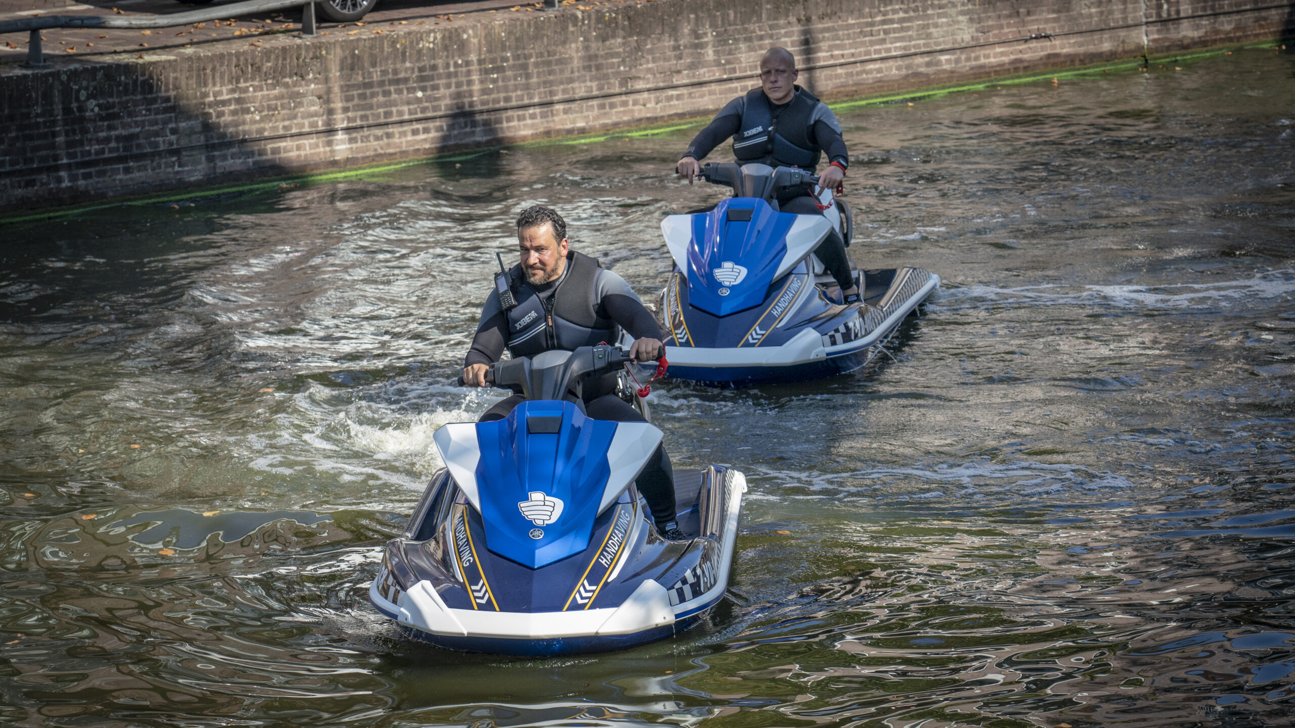 Twee mannen op jetski's in een kanaal.