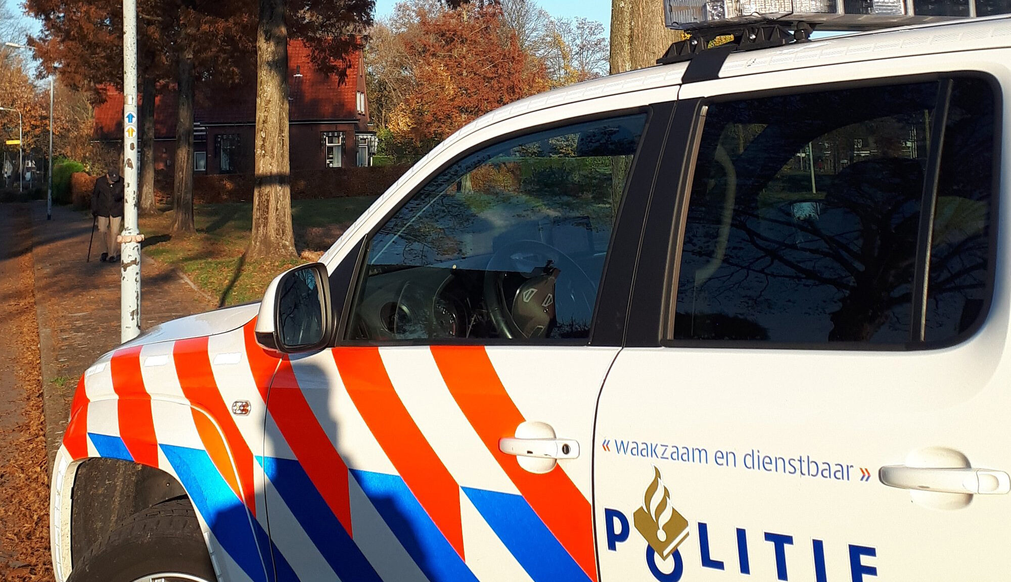 Politieauto geparkeerd naast een trottoir op een zonnige dag, met een gebouw en bomen op de achtergrond.