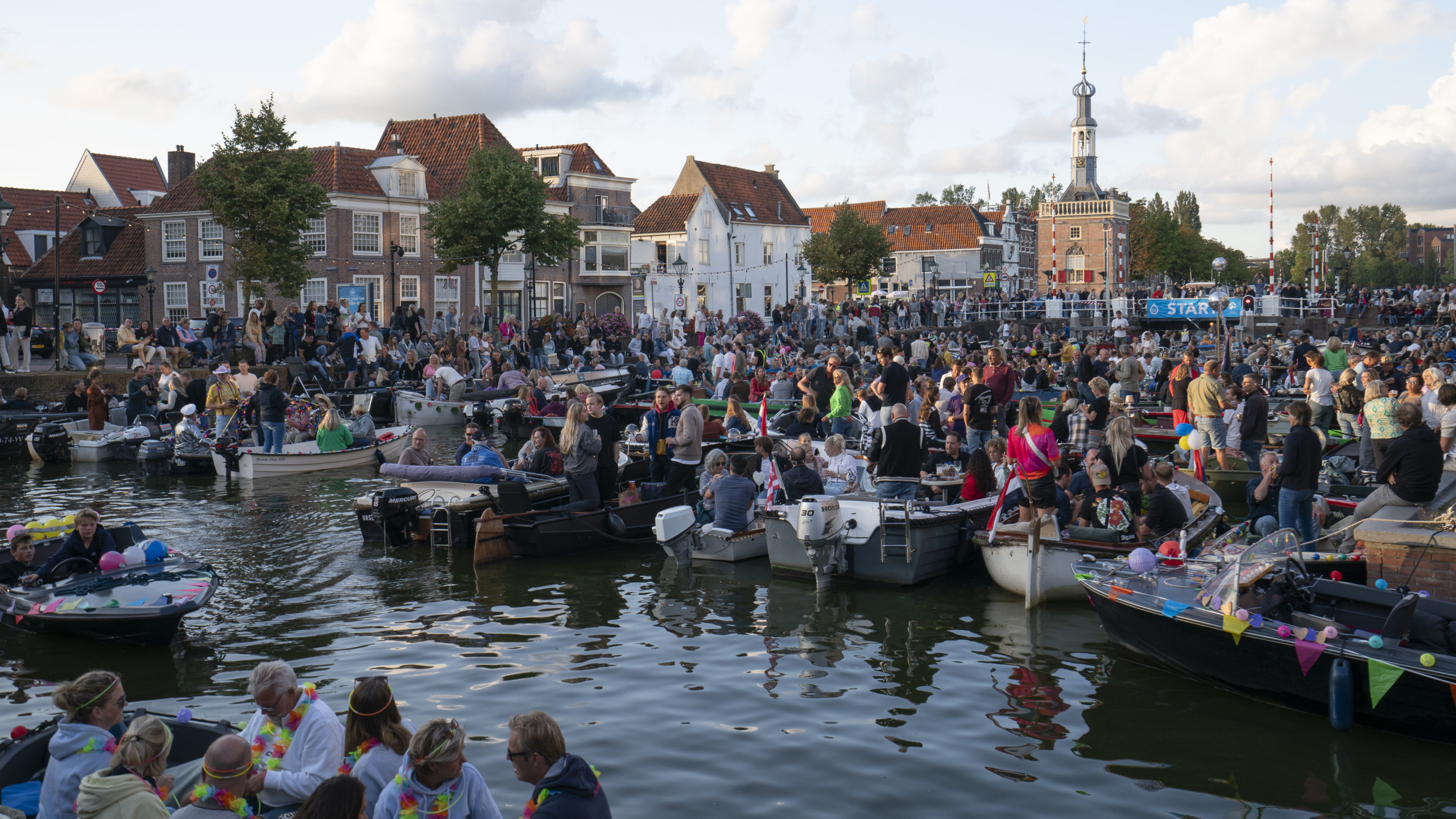 Heel veel mensen in bootjes op het water met een torentje op de achtergrond