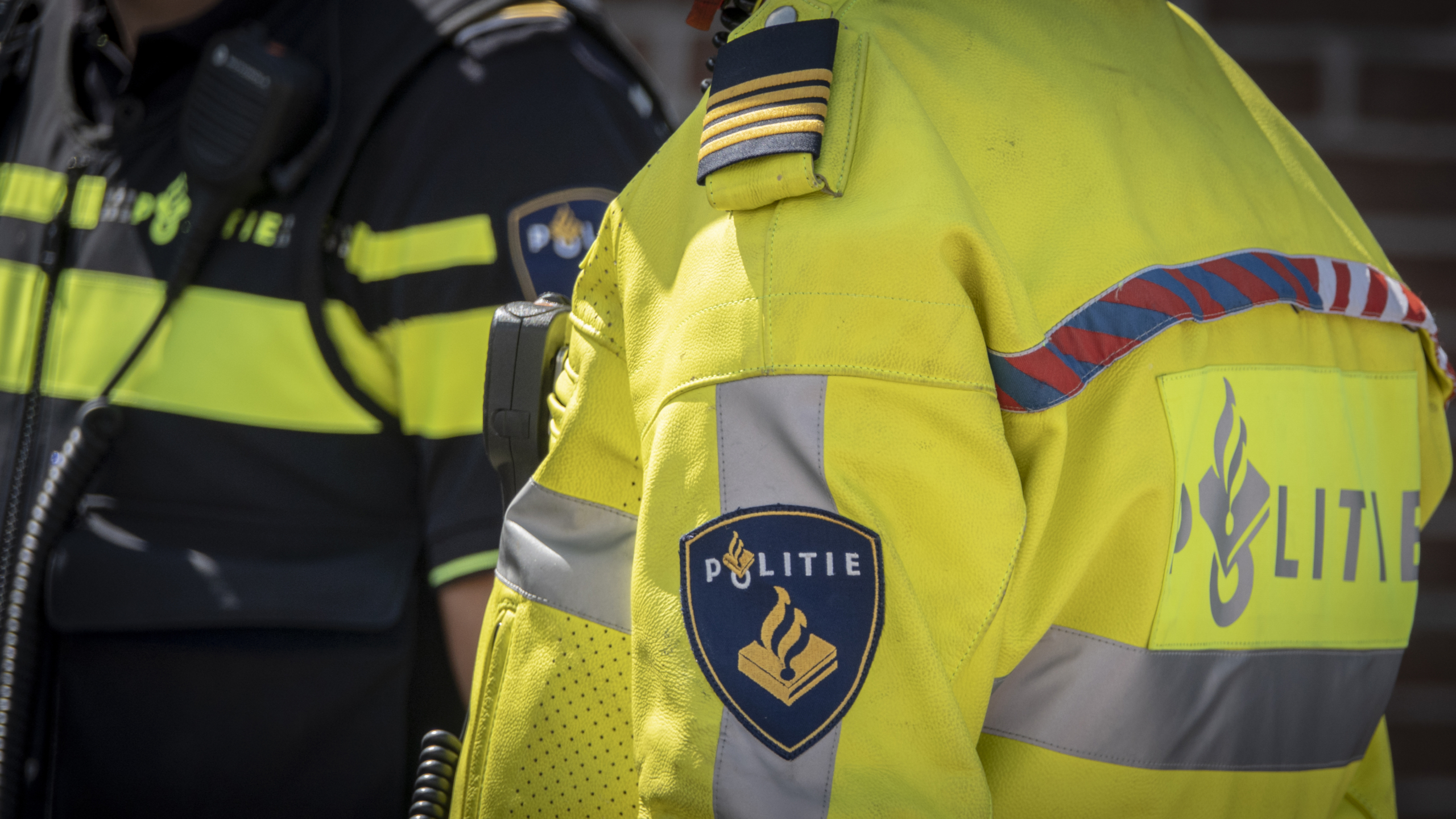 Nederlandse politieagenten in uniform, één in een gele jas en de andere in een donker uniform.