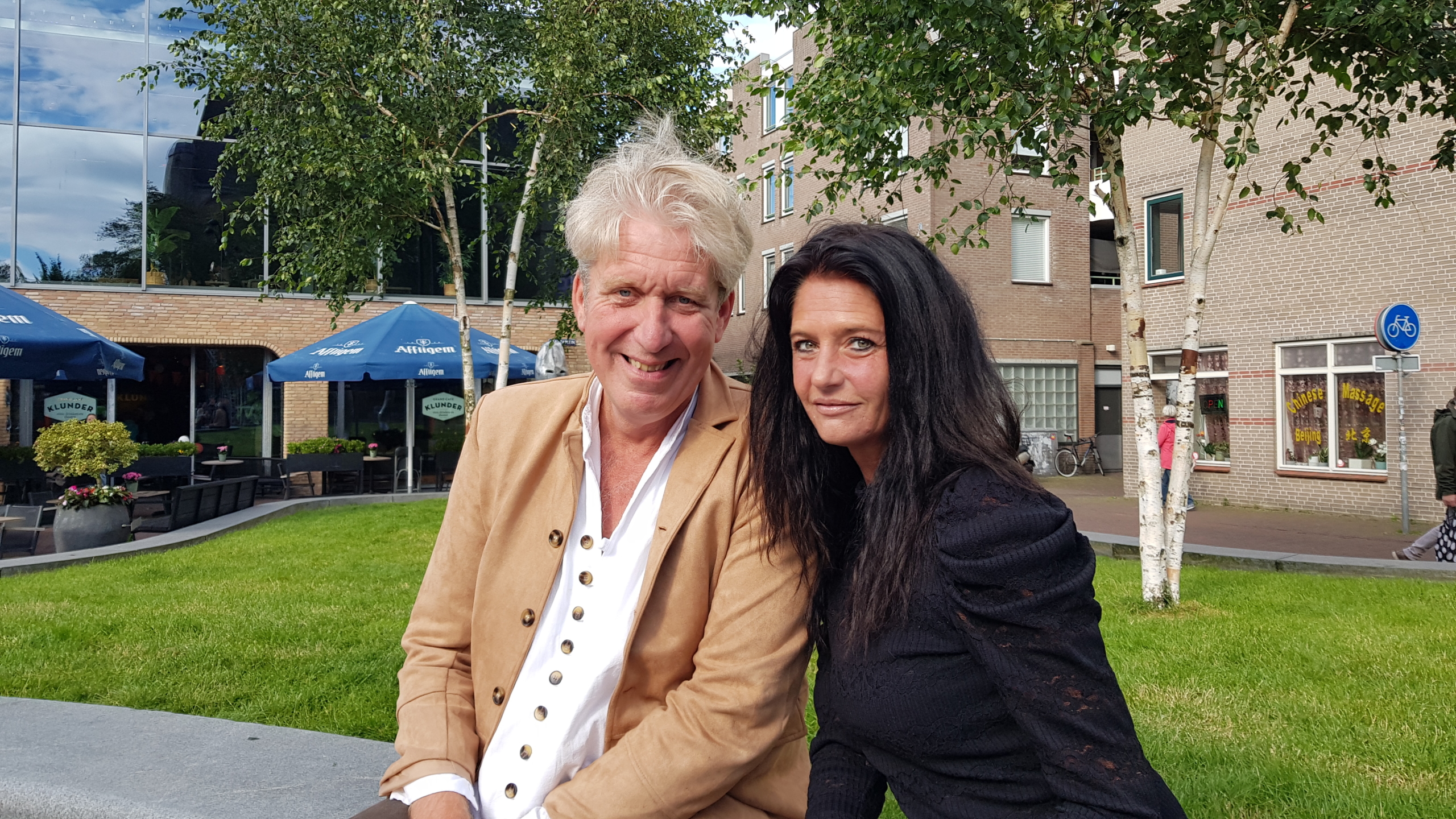 Een man en een vrouw zitten samen op een plein met een terras.