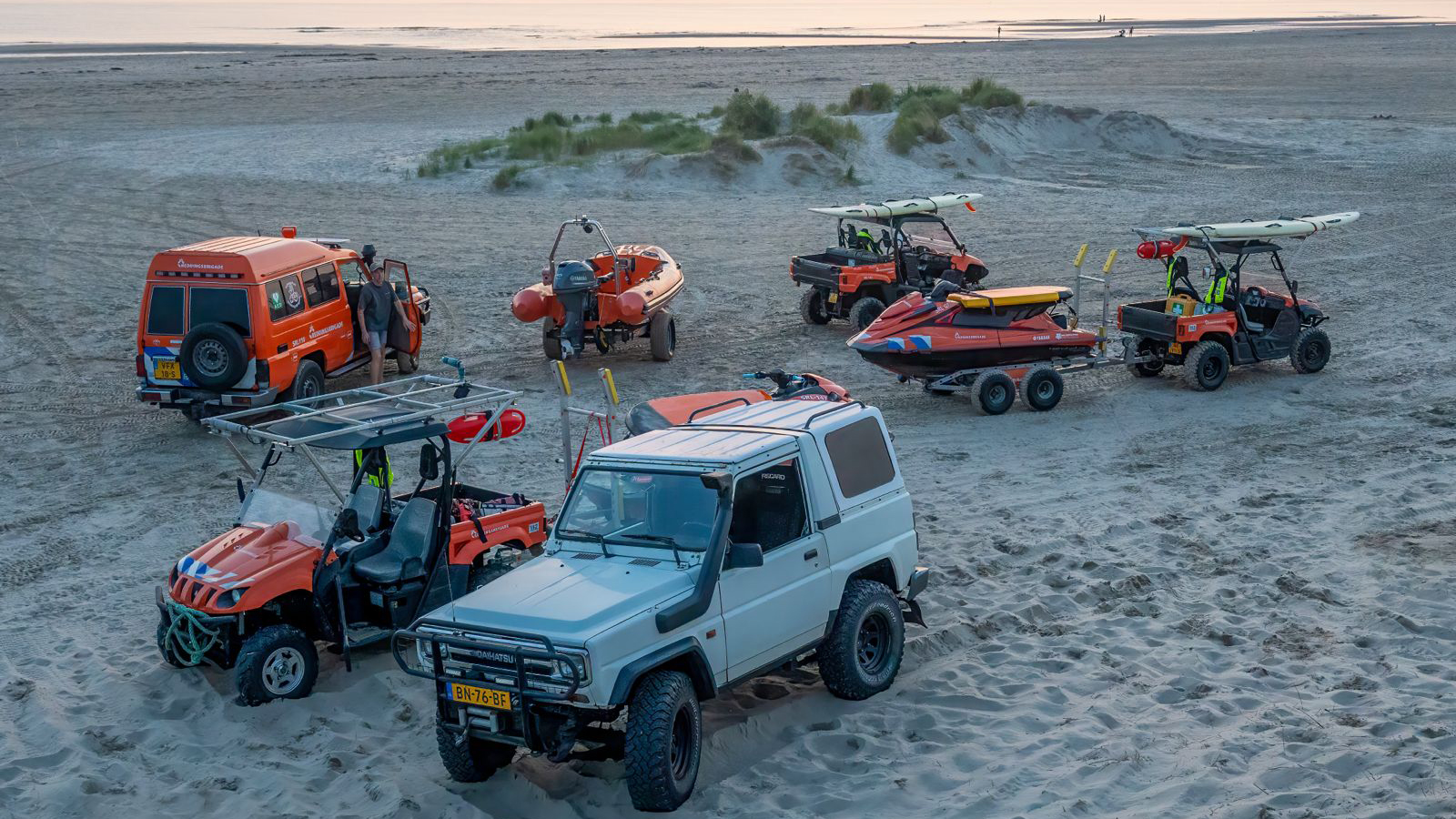 Reddingsvoertuigen op een strand, inclusief een oranje jeep, quads en boten.