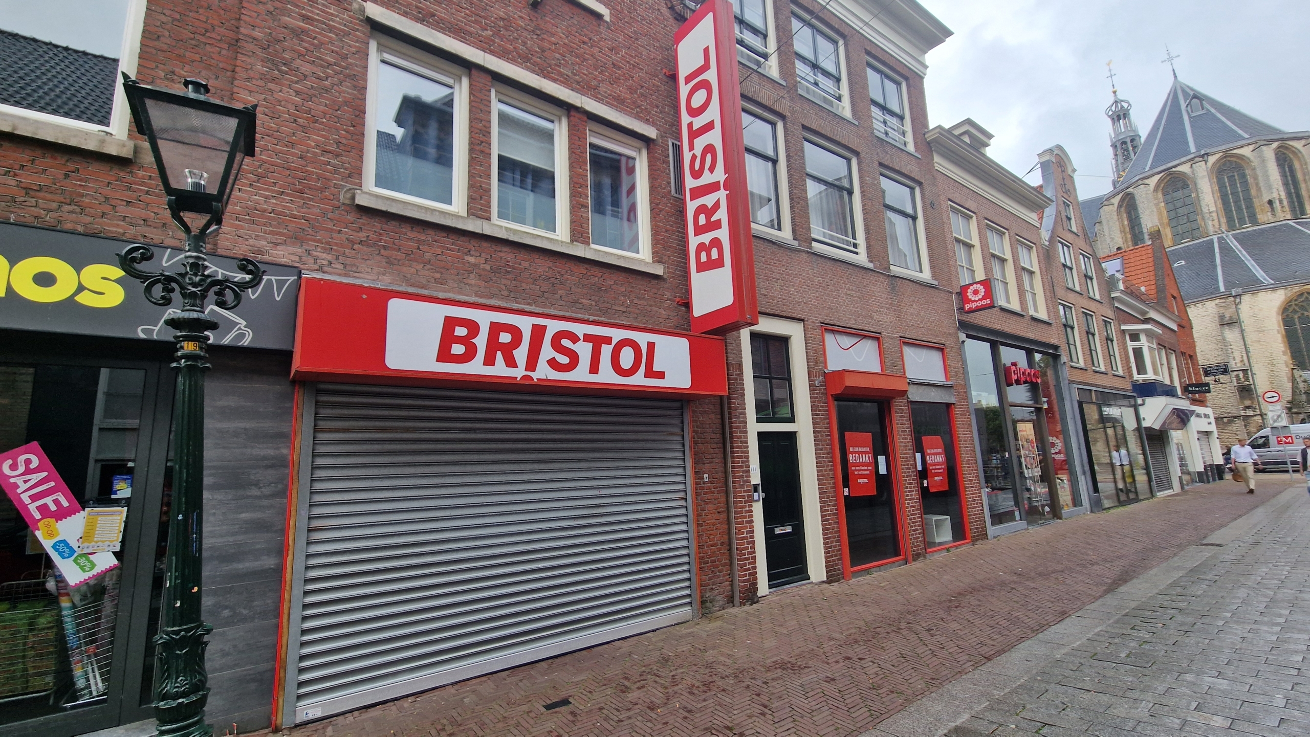 Winkelstraat met de gesloten Bristol winkel, naast verdere winkels en een kerk op de achtergrond.