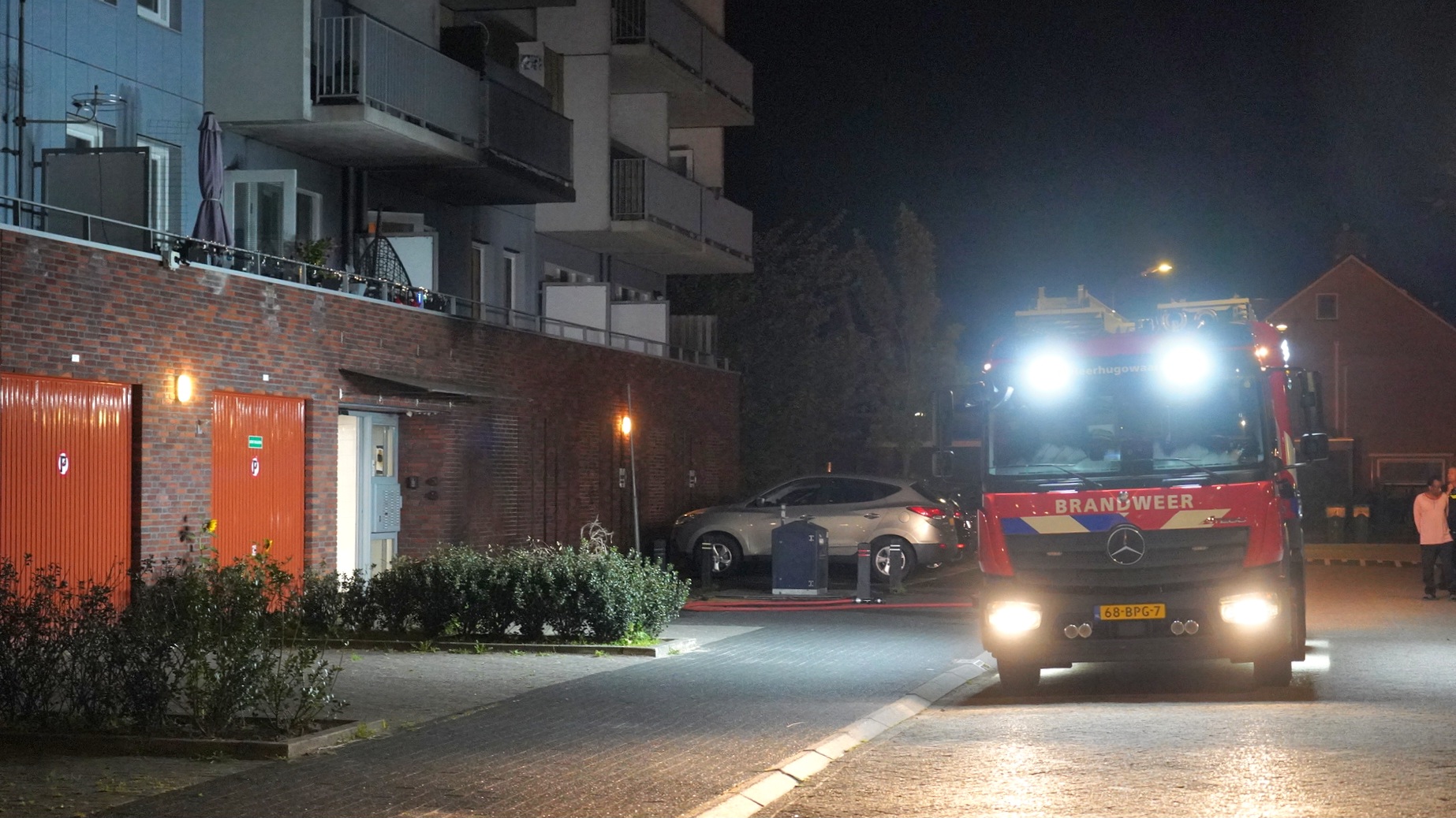 Brandweerwagen bij appartementencomplex in de nacht met felle lichten aan.