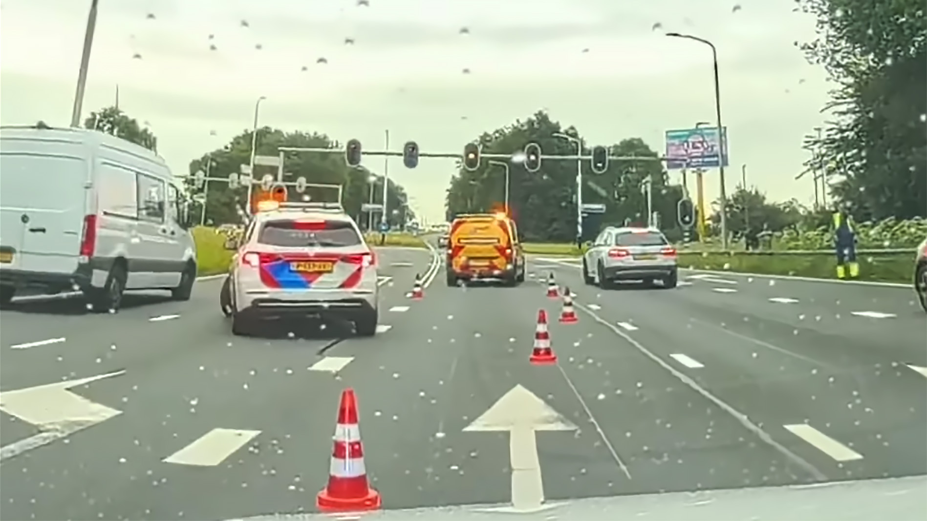 Verkeerssituatie met politieauto, wegafzetting en verkeerskegels op een regenachtige dag.