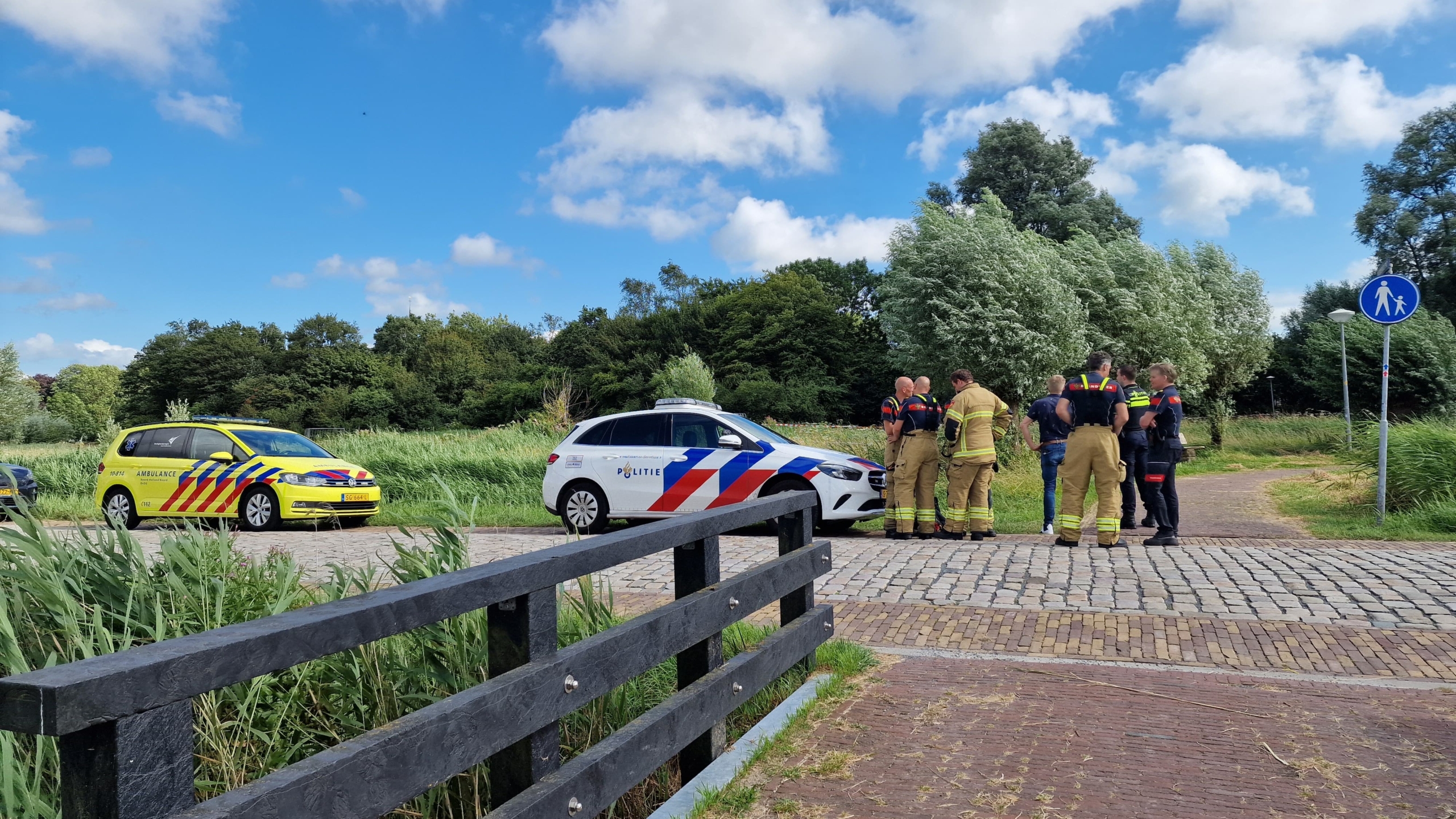 Hulpverleners en twee voertuigen van de politie en ambulance op een landelijke weg.