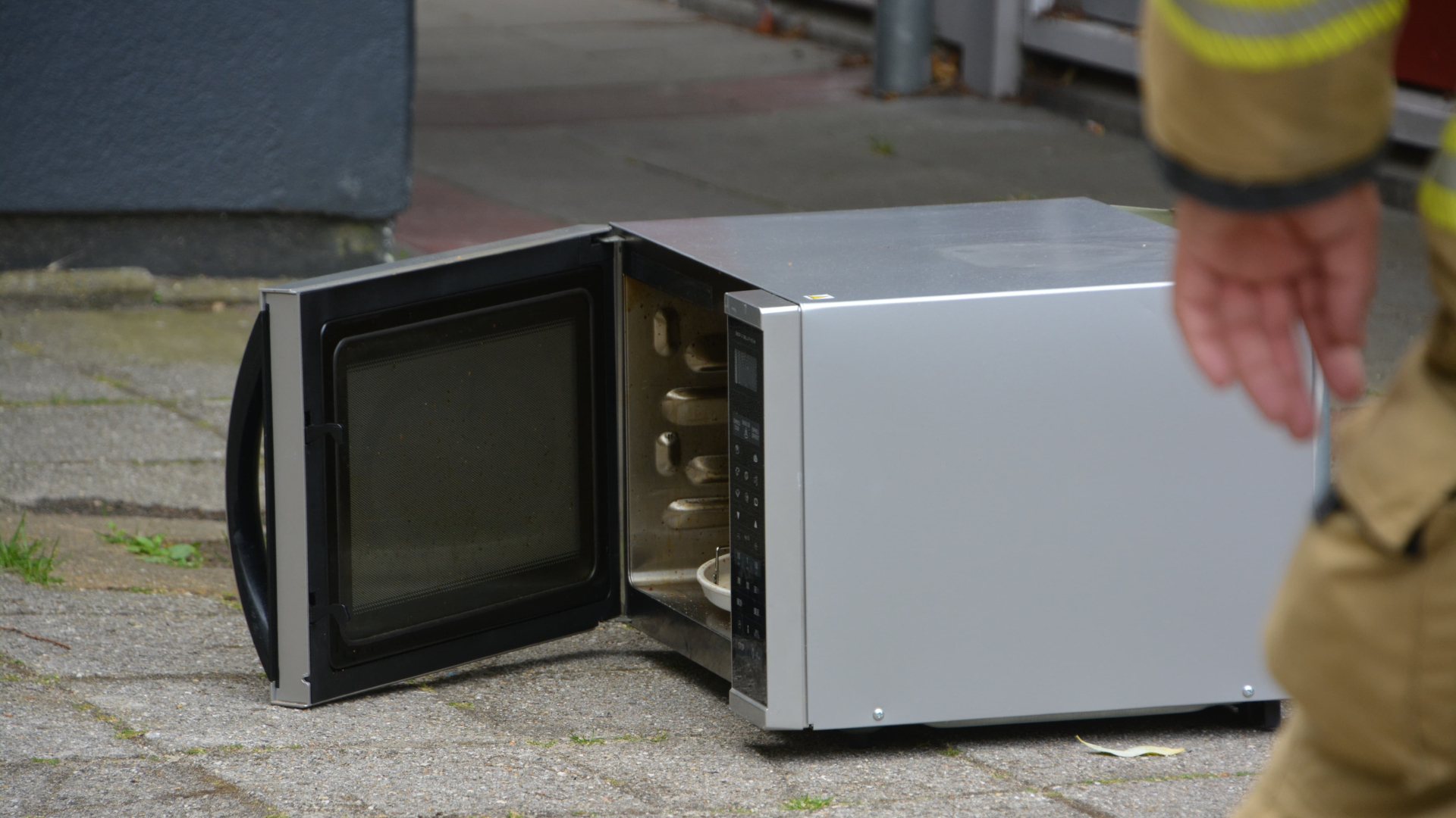 Elektrische oven met open deur op de stoep, naast een persoon in een uniform.