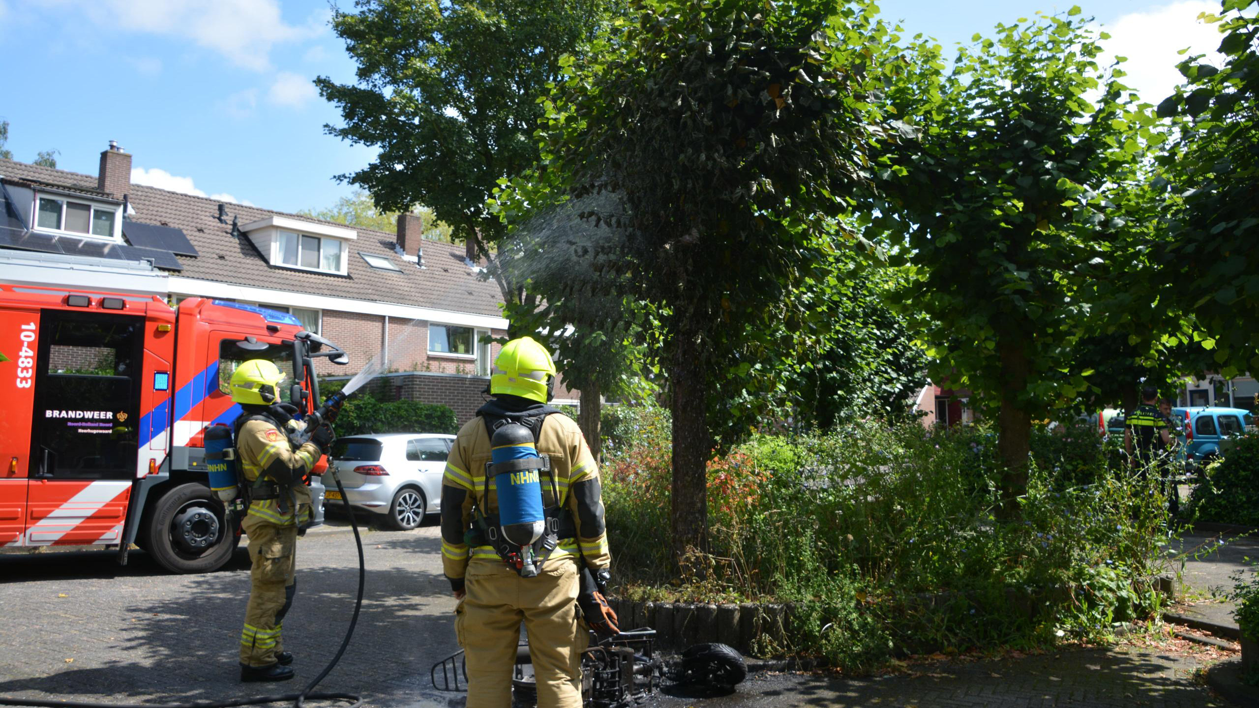 Brandweerlieden die een boom blussen naast een brandweerwagen in een woonwijk.