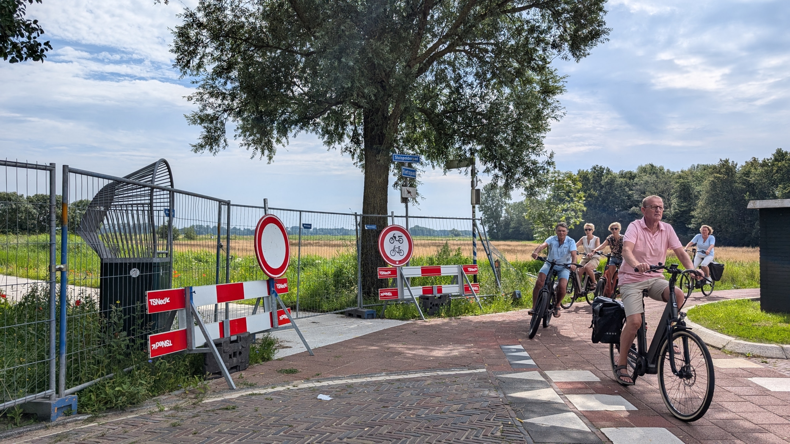 Fietsers rijden langs een afgesloten weg met verkeersborden in een landelijke omgeving.