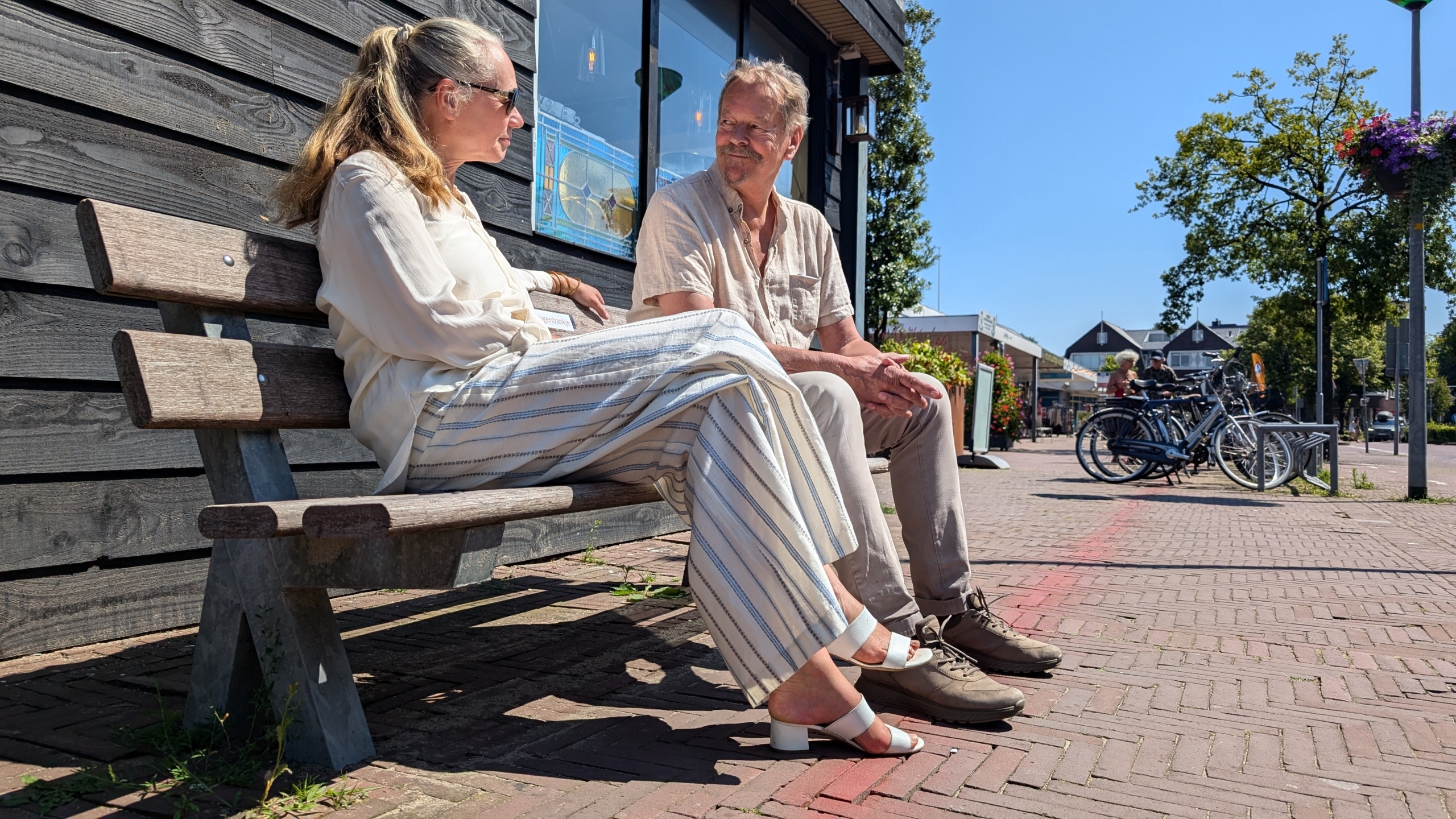 Twee mensen zitten op een bankje buiten op een zonnige dag.