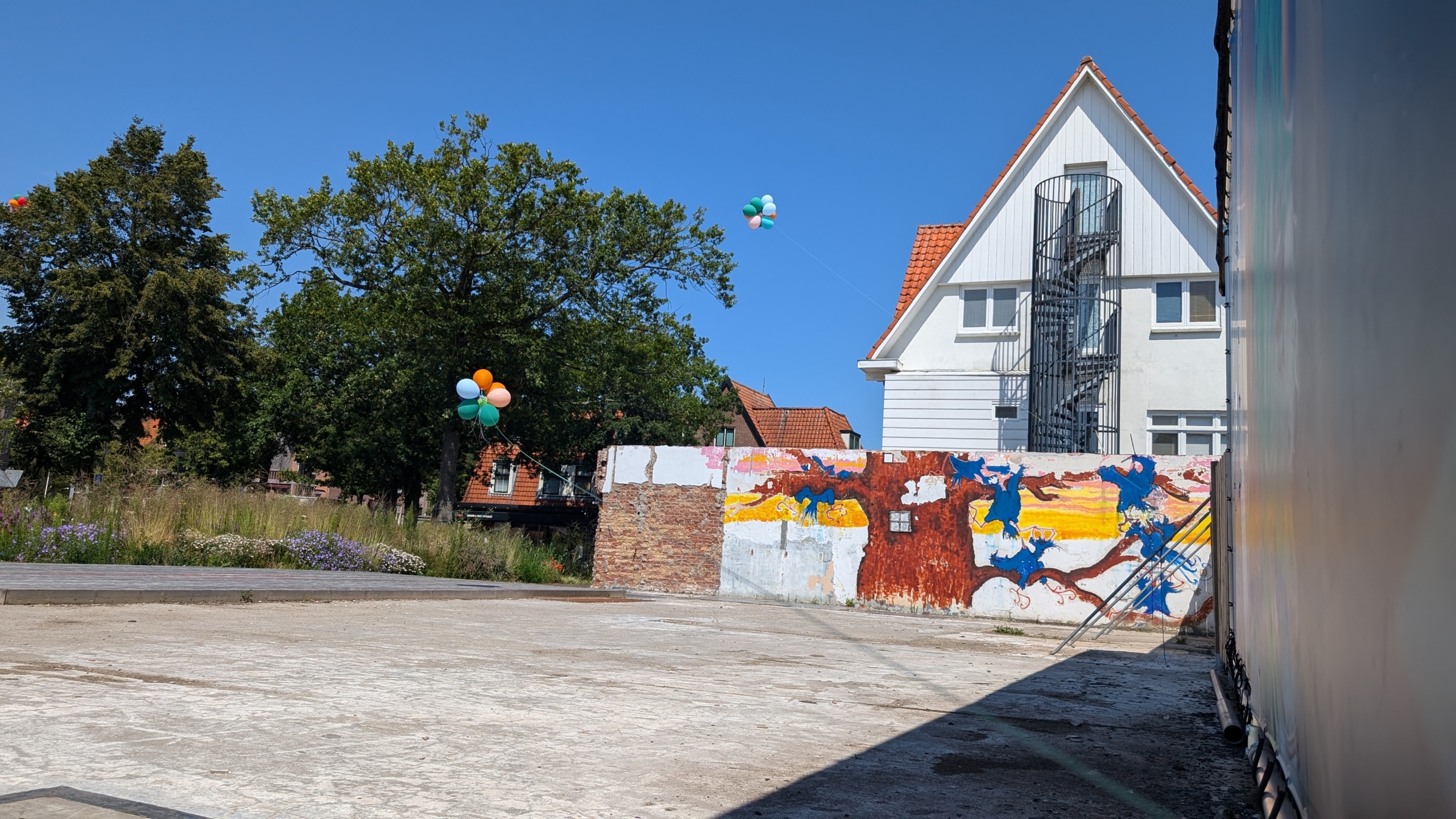 Buitenruimte met een wit huis op de achtergrond, ballonnen in de lucht en een geschilderde muur.