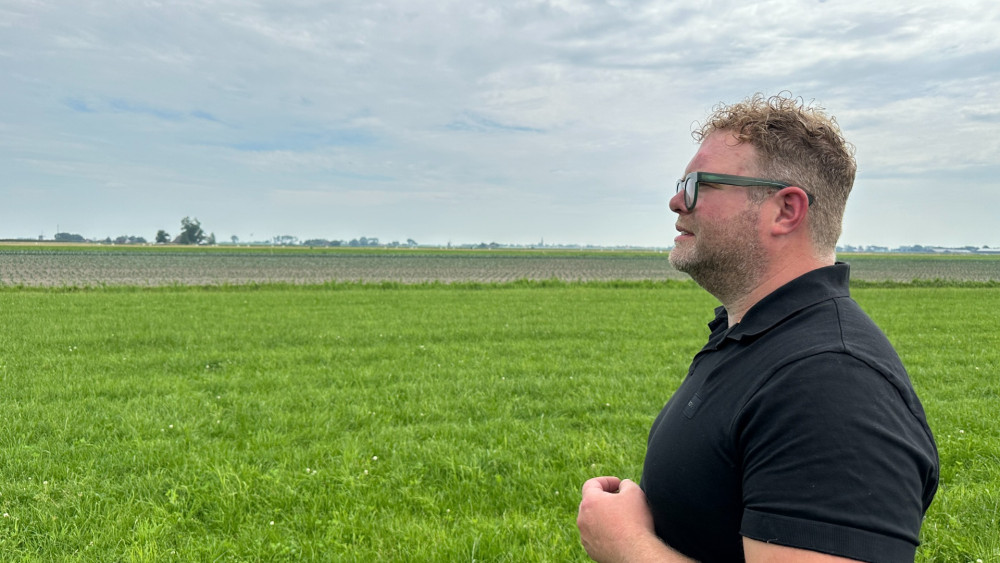 Man in zwarte poloshirt staat in een groen veld en kijkt naar rechts.