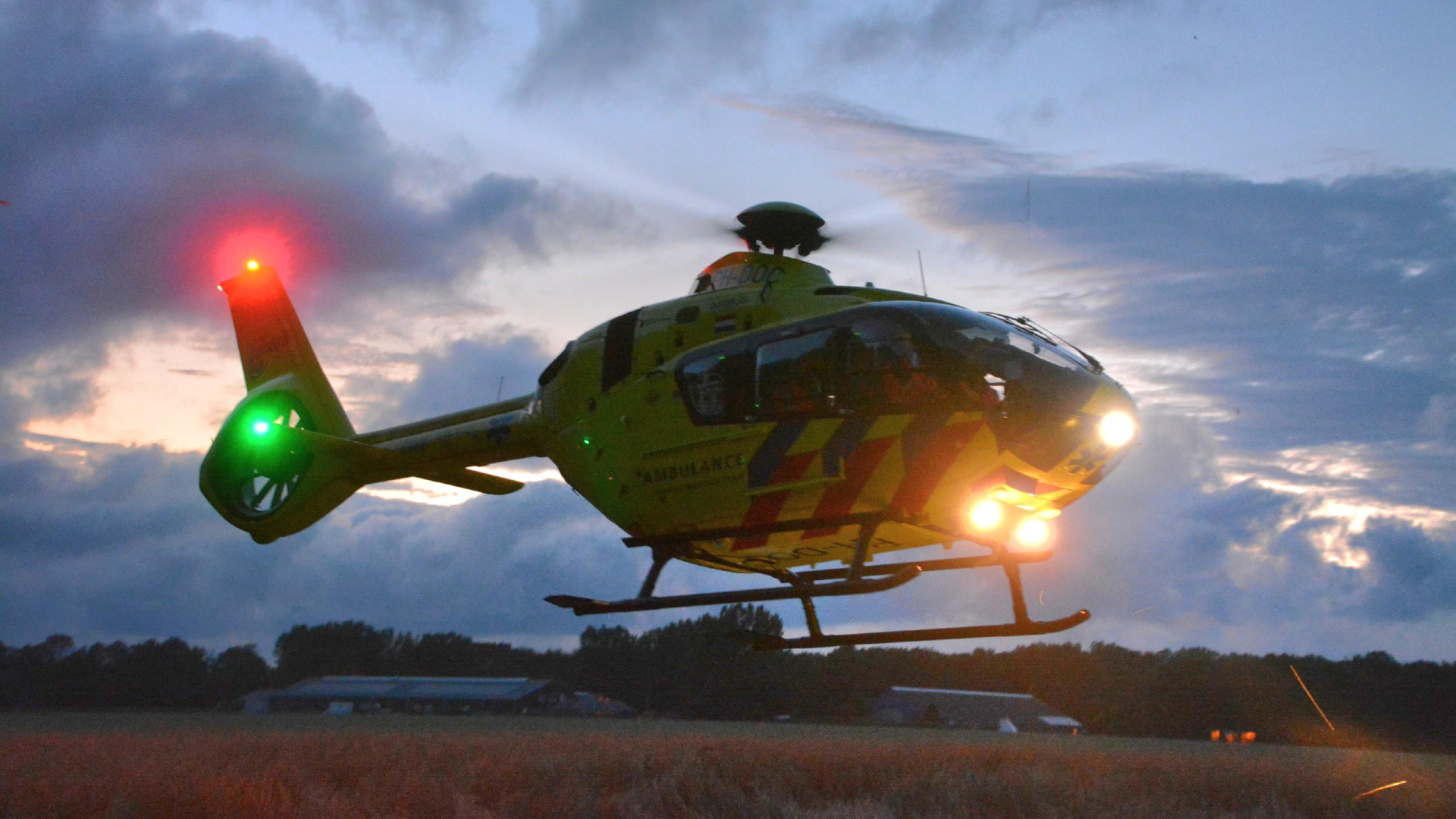 Gele ambulancehelikopter in de lucht bij zonsondergang.