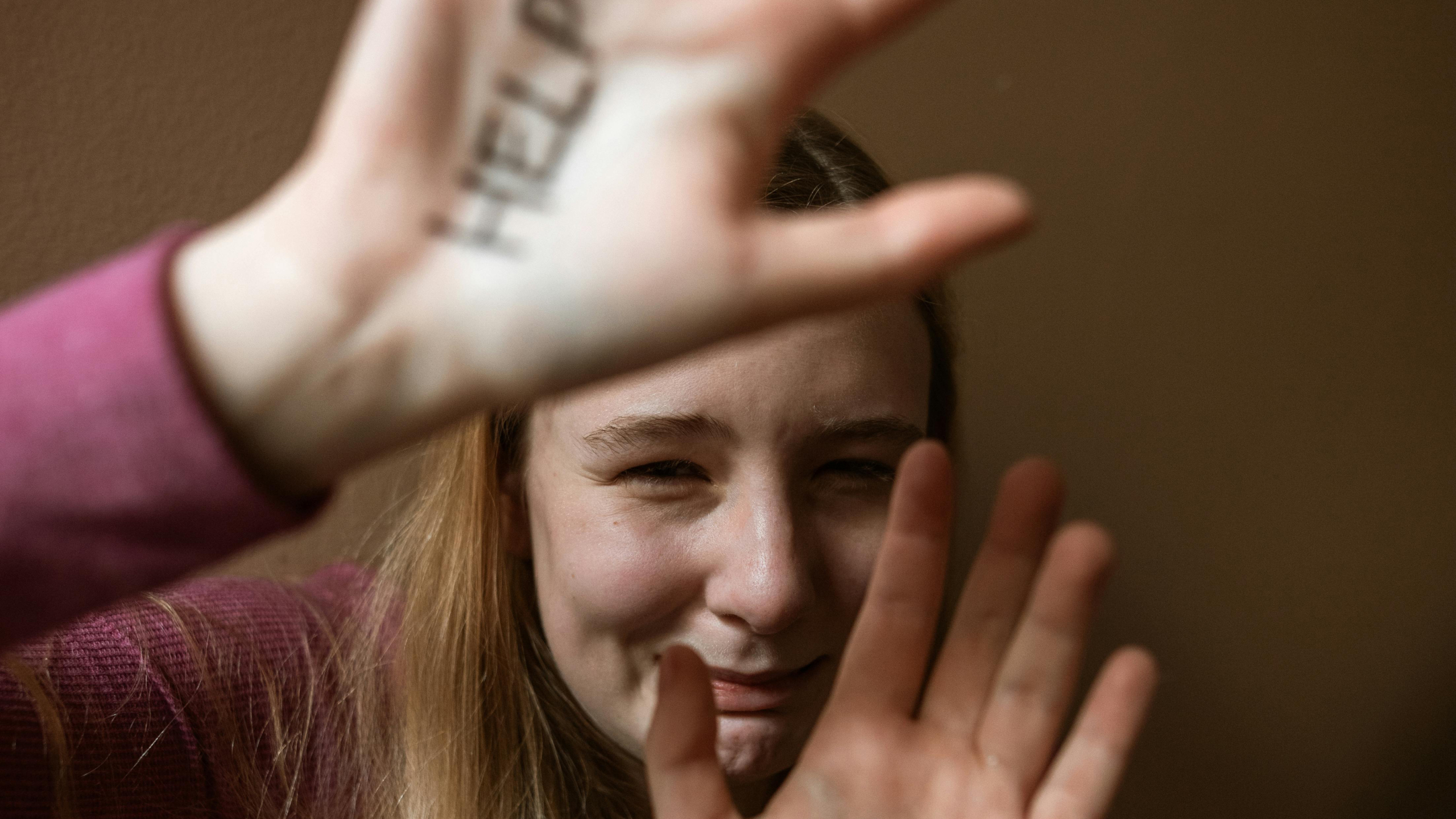 Jonge vrouw huilt en bedekt haar gezicht met haar handen; op één hand staat het woord HELP geschreven.