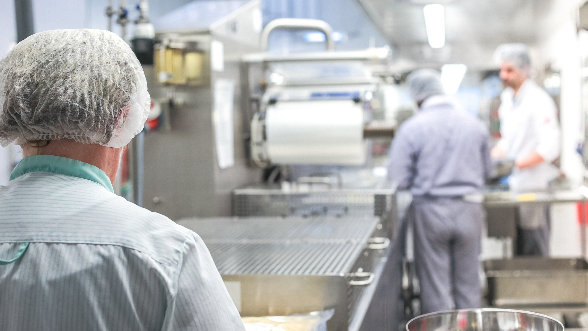 Mensen werken in een industriële keuken met haarnetjes en schorten aan.