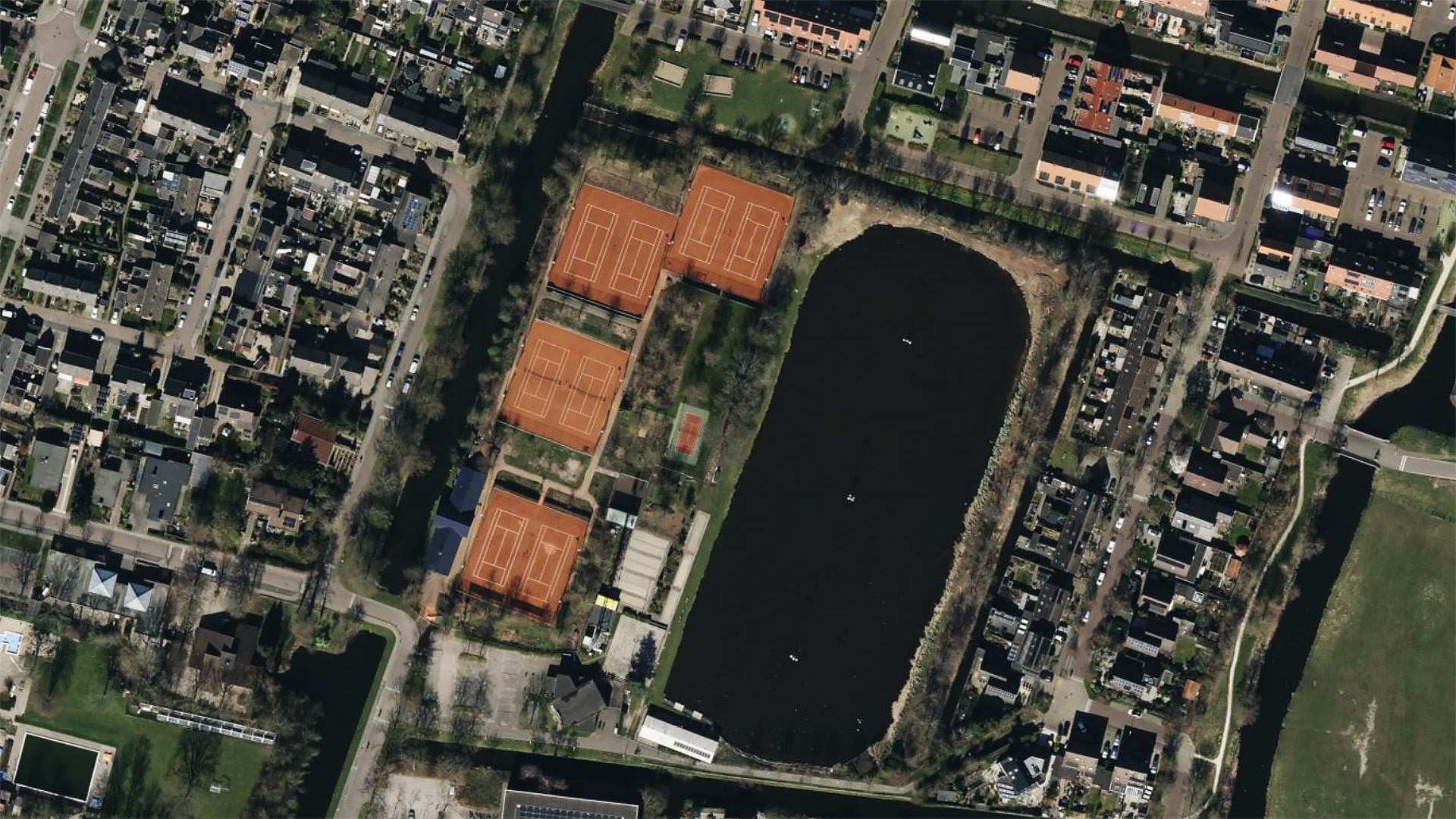 Luchtfoto van een woonwijk met tennisbanen en een groot vijver.