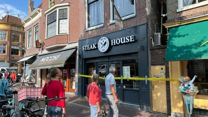 Mensen staan voor een afgesloten steakhouse met politielint aan de straatkant.