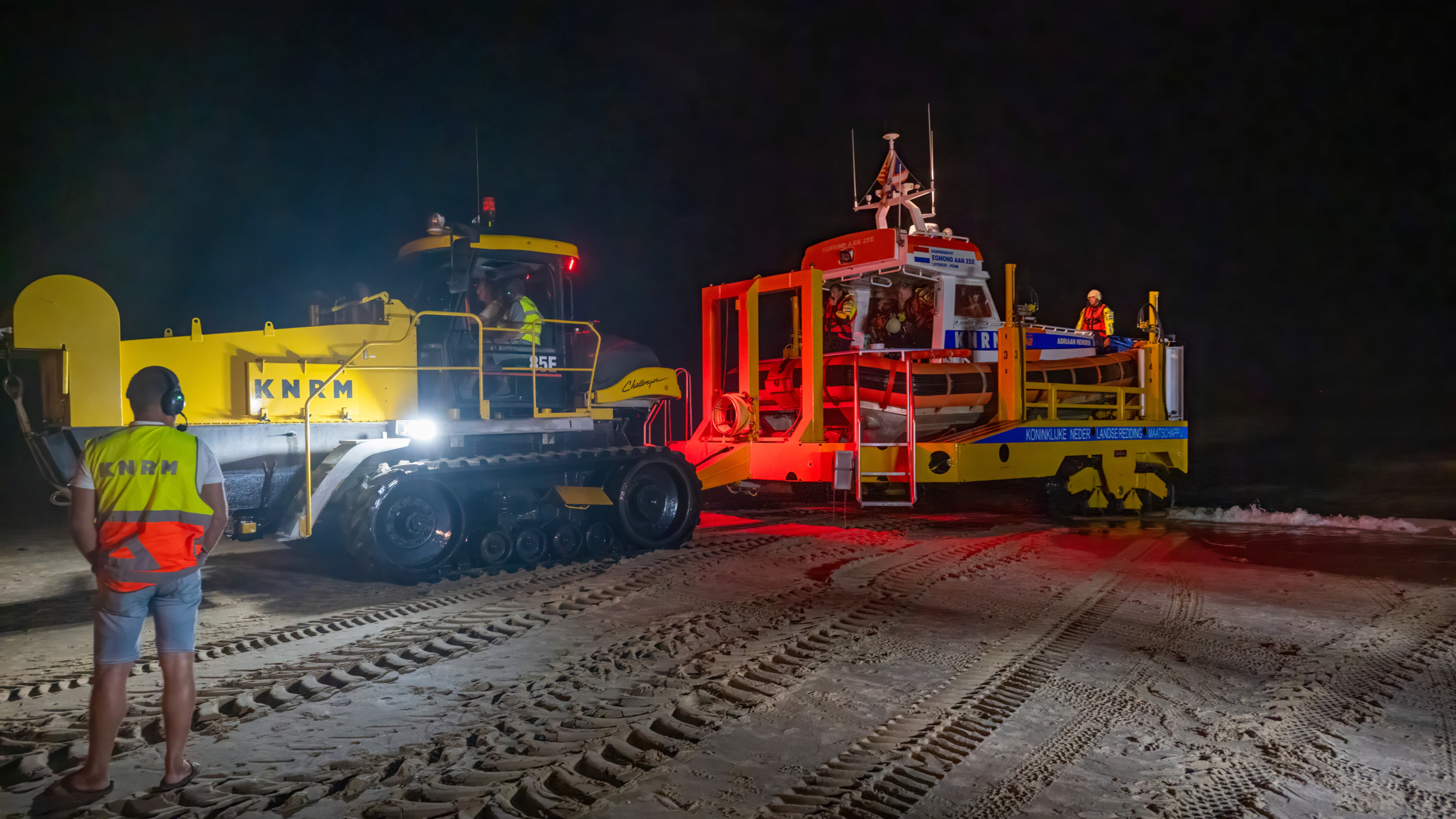 Reddingsvoertuig van de KNRM rijdt 's nachts het strand op, met een bemanningslid op de voorgrond.