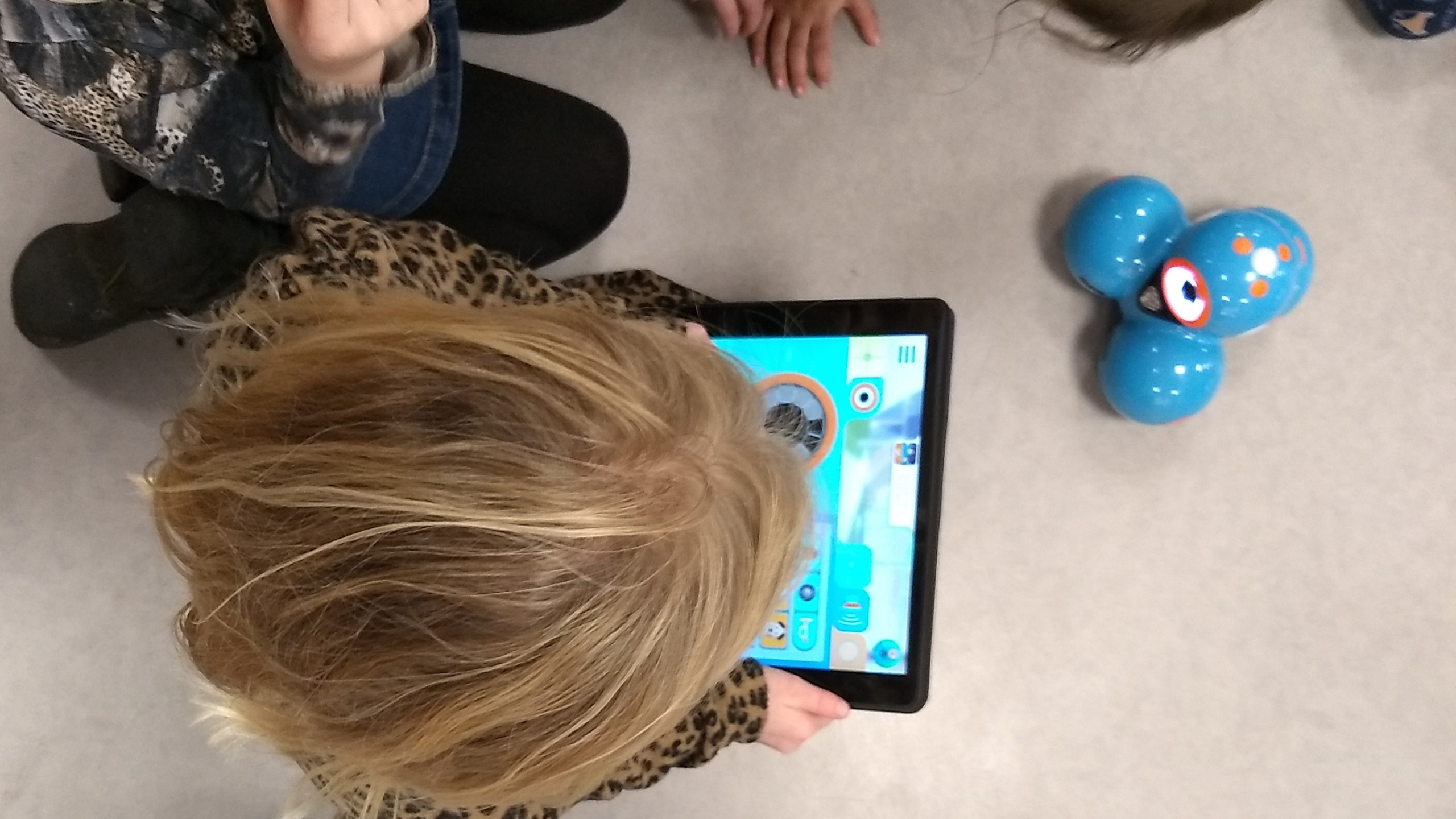 Kinderen spelen met een tablet en een blauwe robot.