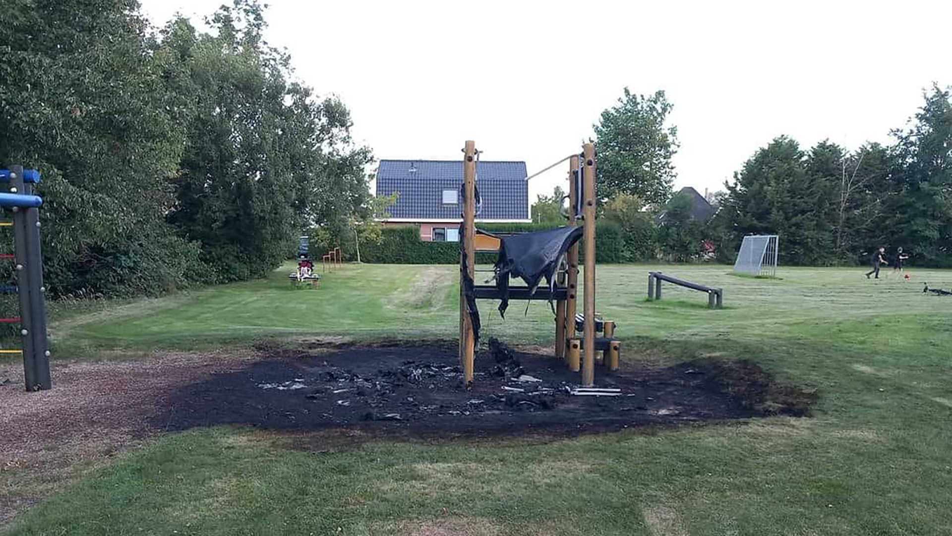 Verbrand speeltoestel in een park met gras en bomen op de achtergrond.