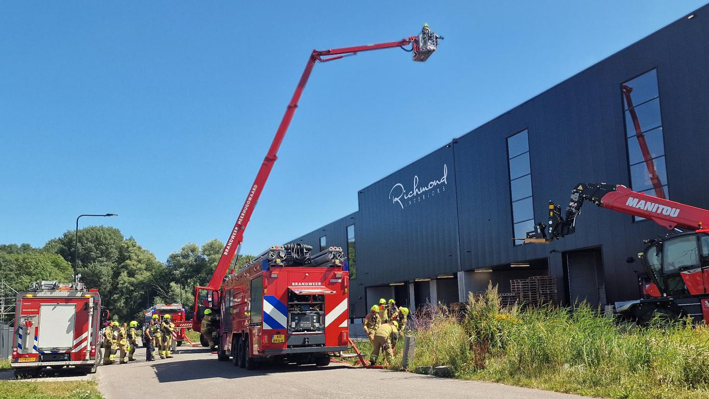 Brandweerwagens en brandweerlieden bij een industrieel gebouw met de tekst "Richmond Interiors".