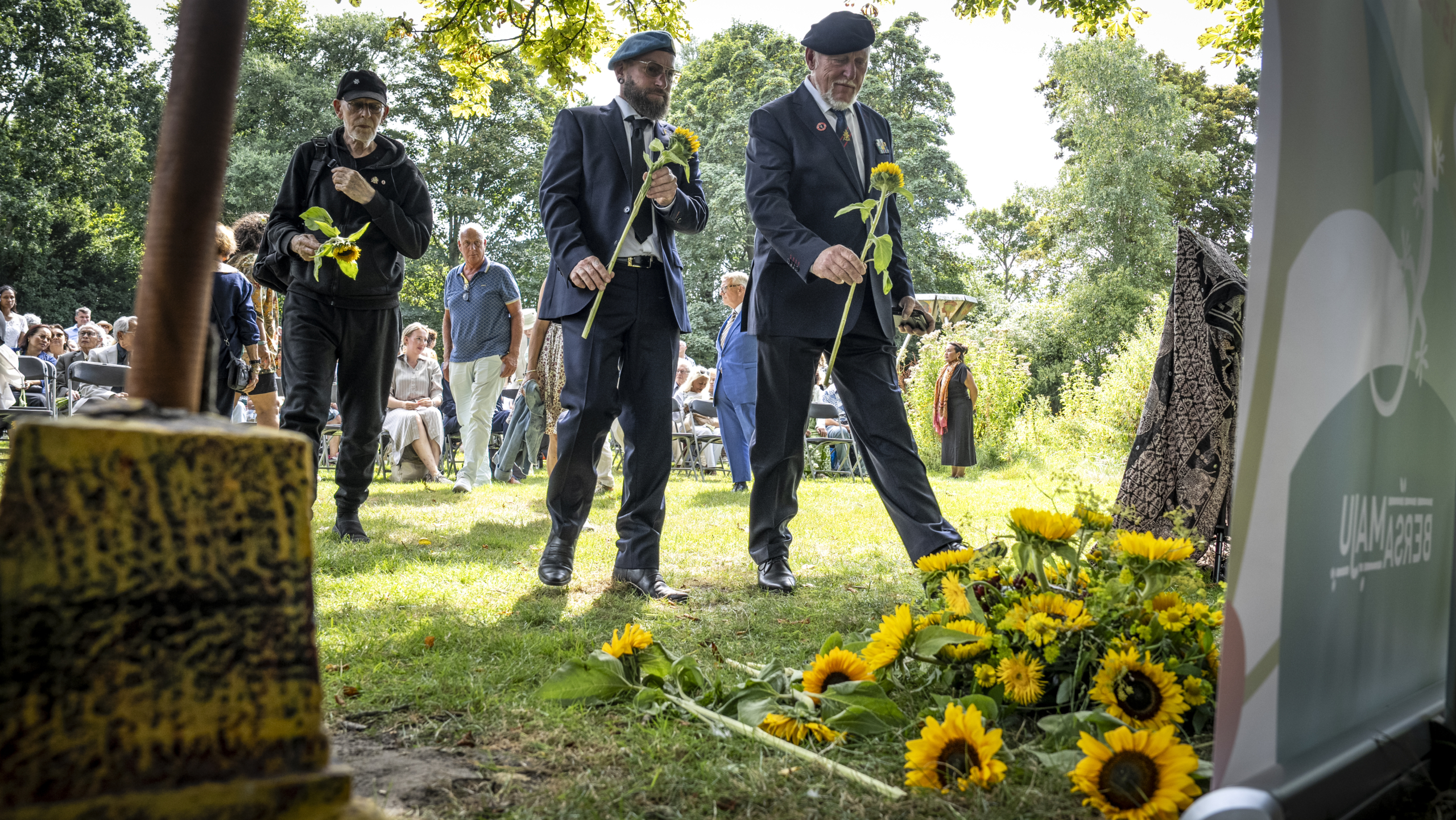 Mensen leggen zonnebloemen neer tijdens een herdenkingsceremonie buiten.