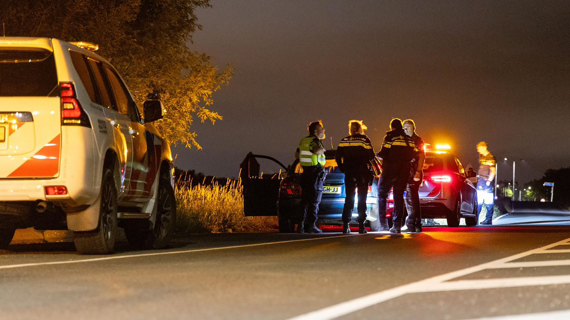 Politieagenten staan 's nachts bij twee auto's langs de kant van de weg.