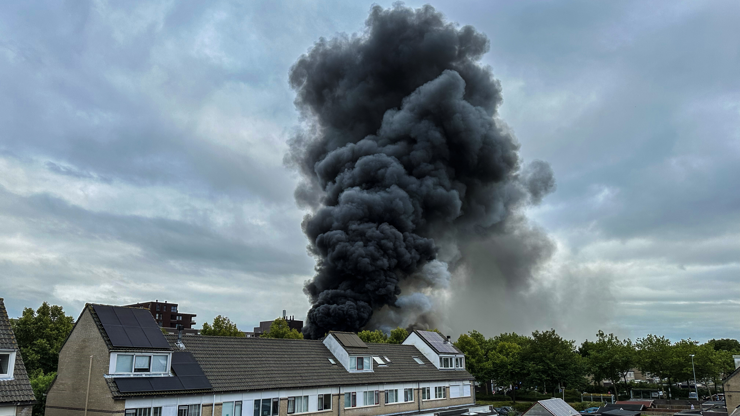 Een grote zwarte rookwolk stijgt op boven een woonwijk met huizen met dakpannen.