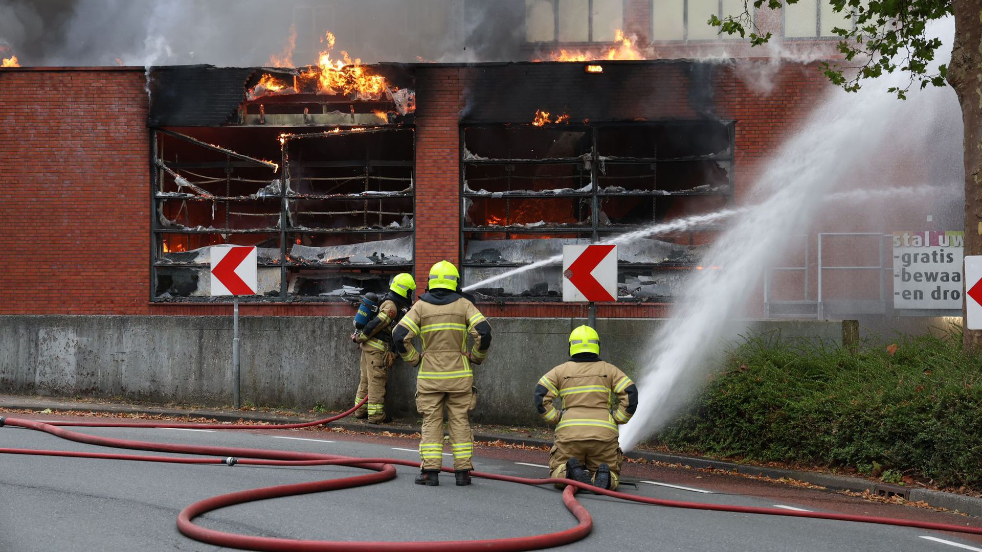 Brandweerlieden bestrijden een grote brand in een gebouw met brandslangen en waterstralen.