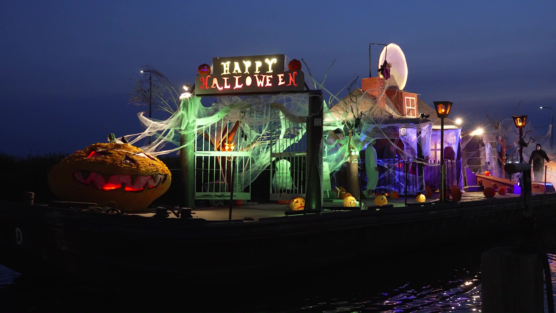 Helloween-decoratie op een drijvend platform met een groot bord "Happy Halloween", spinnenwebben en een verlichte pompoen.