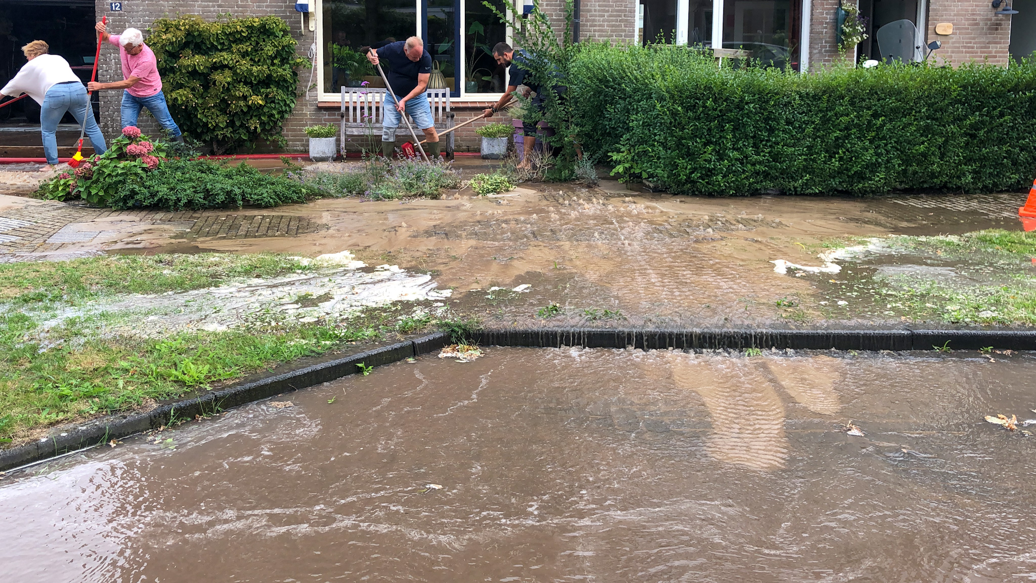 Mensen proberen water uit hun overstroomde tuin weg te halen met bezems.