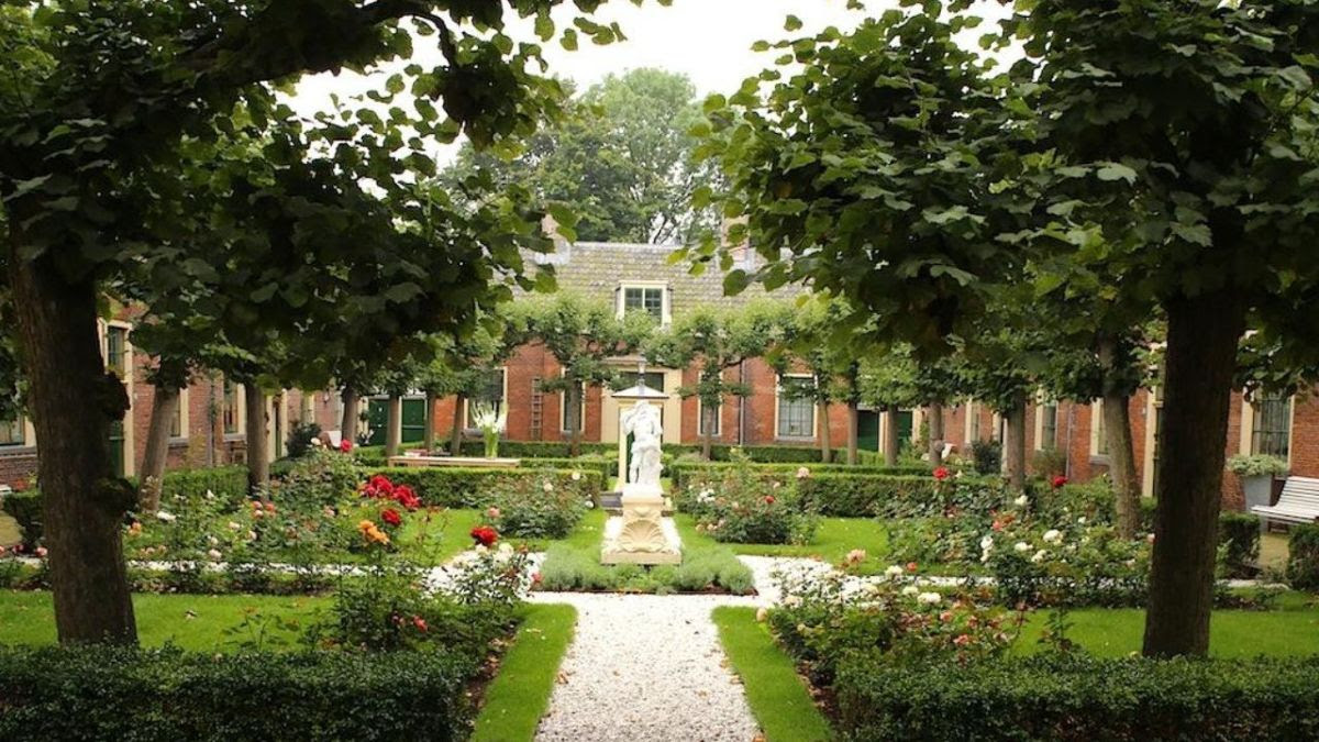 Binnenplaats met goed onderhouden tuin, bloemenperken, bomen en een standbeeld, omgeven door traditionele bakstenen gebouwen.