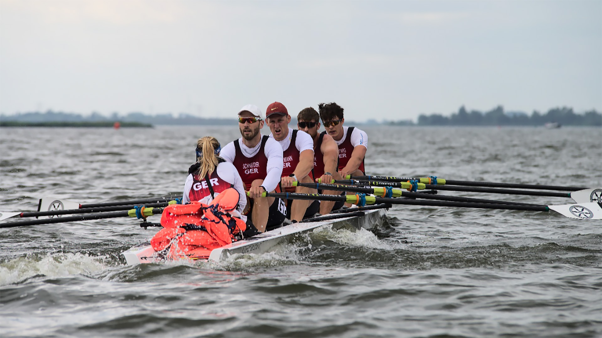 Roeiteam met vier roeiers en een stuurman op open water, gekleed in uniformen met opschrift 'GER'.