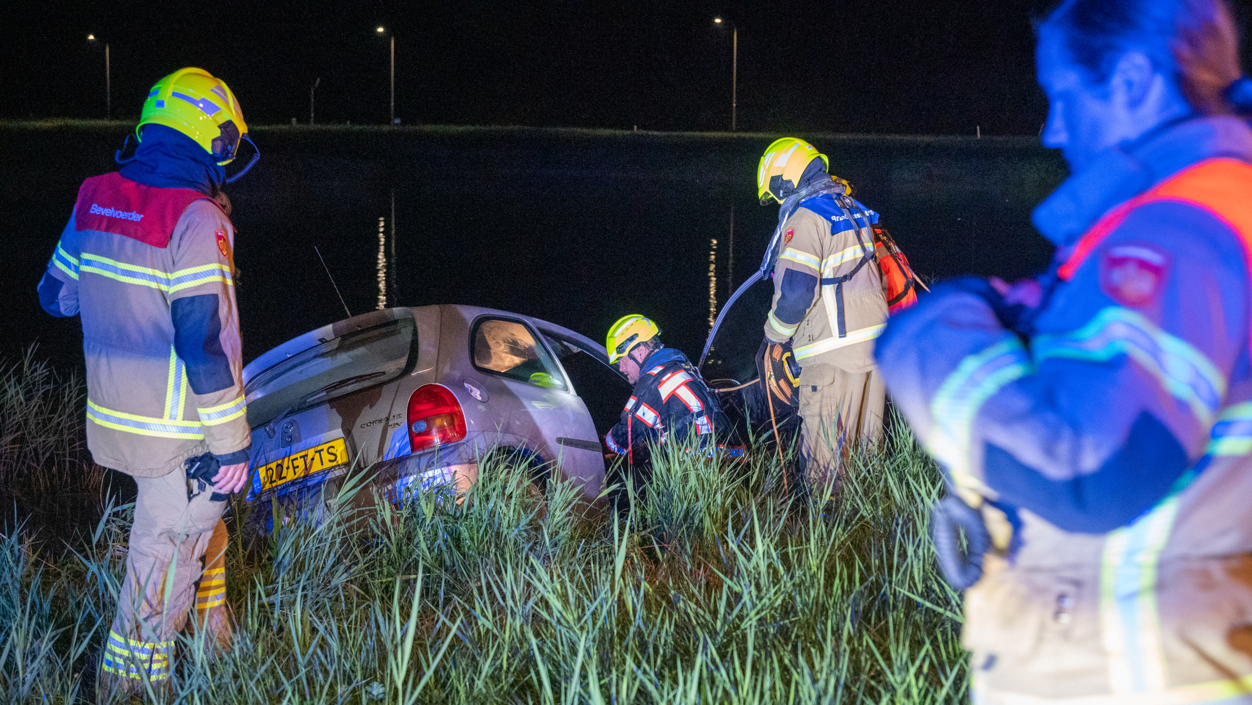 Brandweerlieden redden auto uit sloot in het donker.