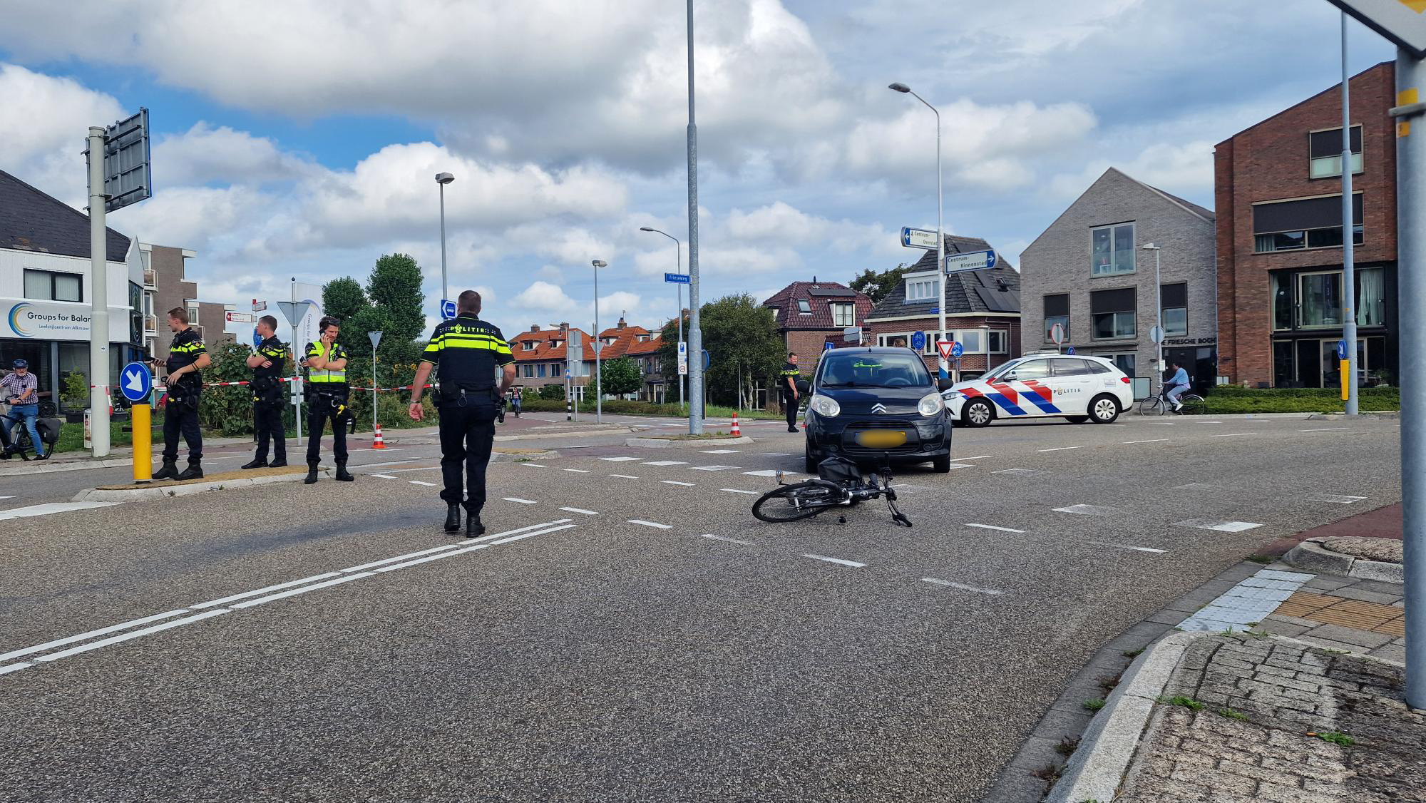 Politieagenten onderzoeken een verkeersongeval met een fiets en een auto op een kruispunt.