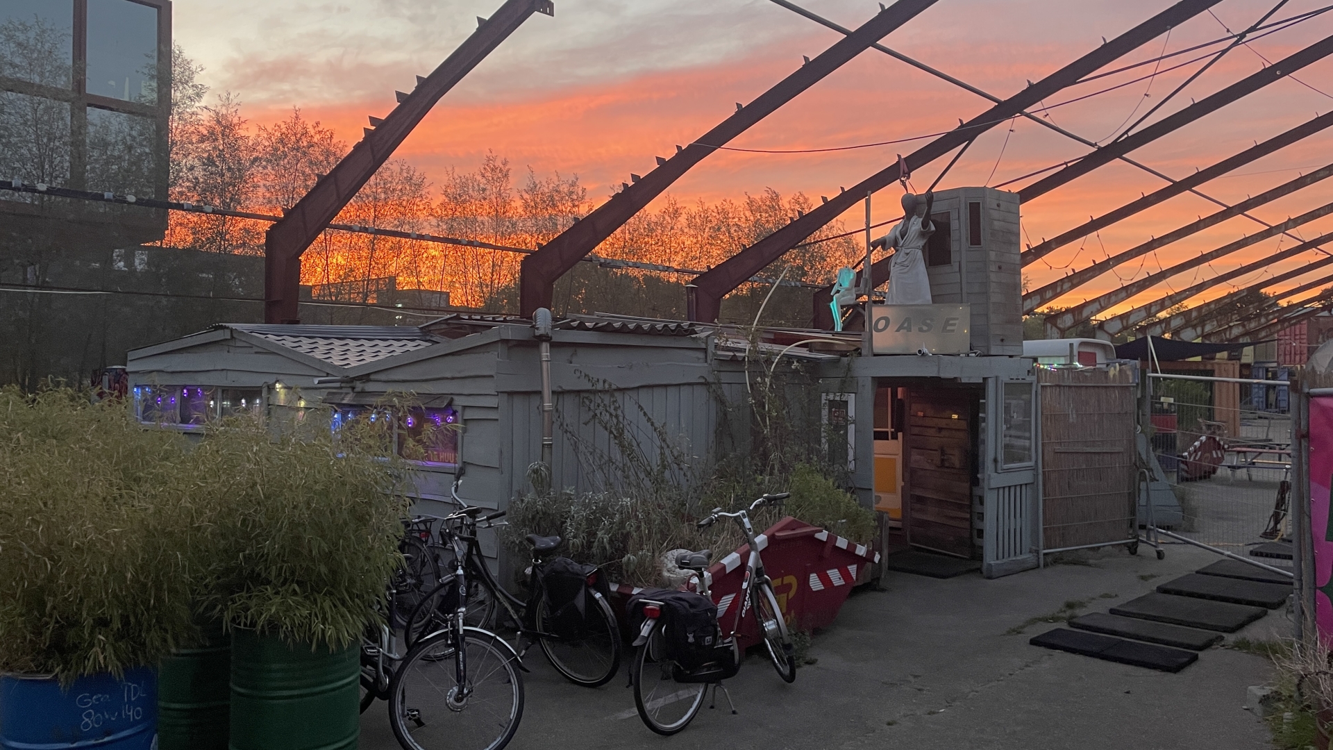 Zonsondergang met een gebouw gemarkeerd als "Oase" en verschillende fietsen op de voorgrond.