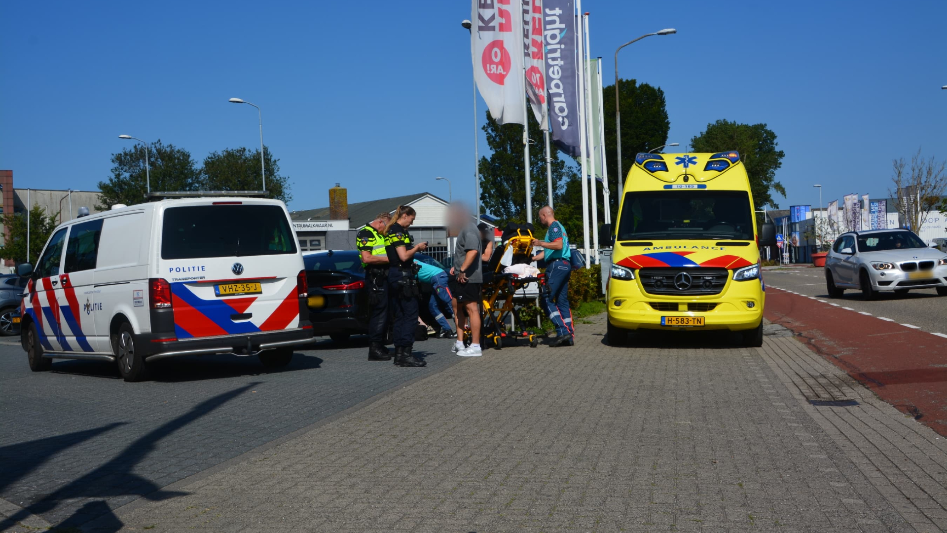 Politieagenten en medisch personeel assisteren bij een incident op straat tussen een politievoertuig en een ambulance.