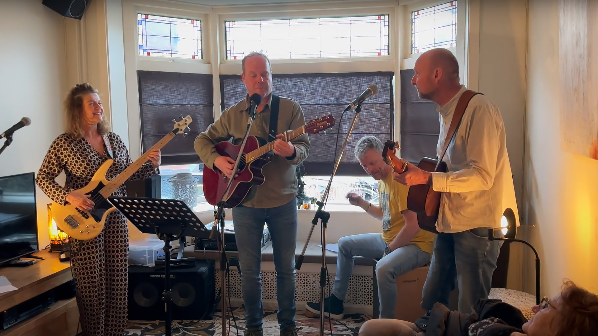 Band die oefent in een woonkamer met een bassist, twee gitaristen en een cajón-speler.