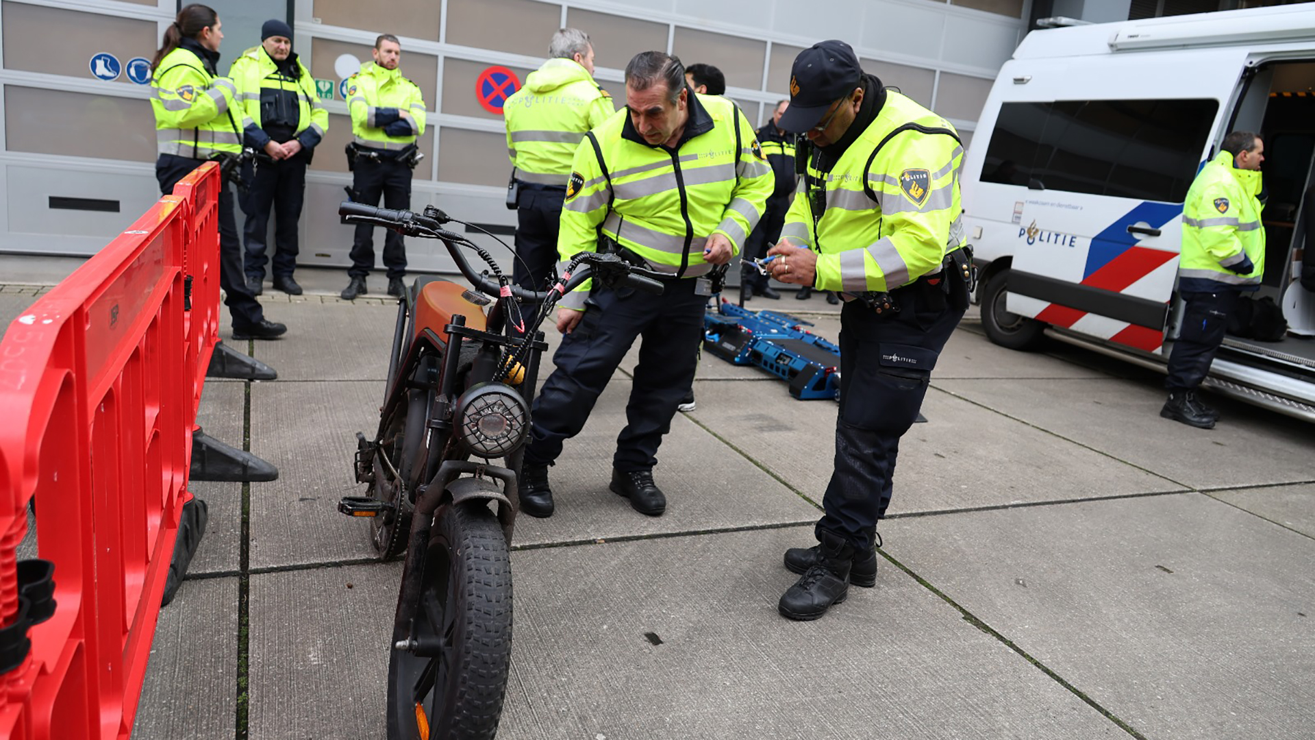 Politieagenten inspecteren een fiets naast een busje van de politie.