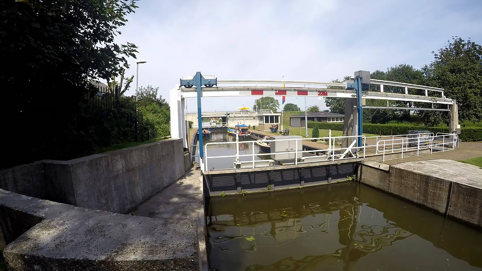 Sluis met geopende poort, verschillende boten en een brug in de verte.