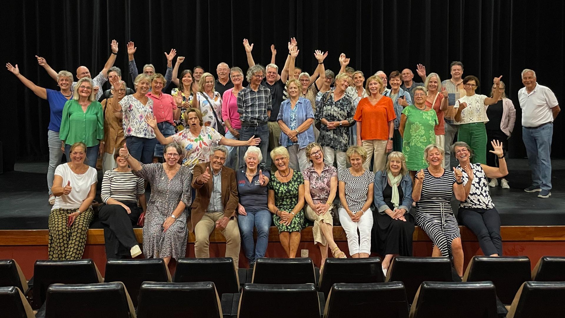 Een groep van meer dan vijftig mensen poseert enthousiast op een podium, waarbij enkele mensen in de voorste rij zitten en de anderen achter hen staan.