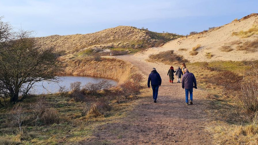 Mensen wandelen op een zandpad door een duinlandschap.