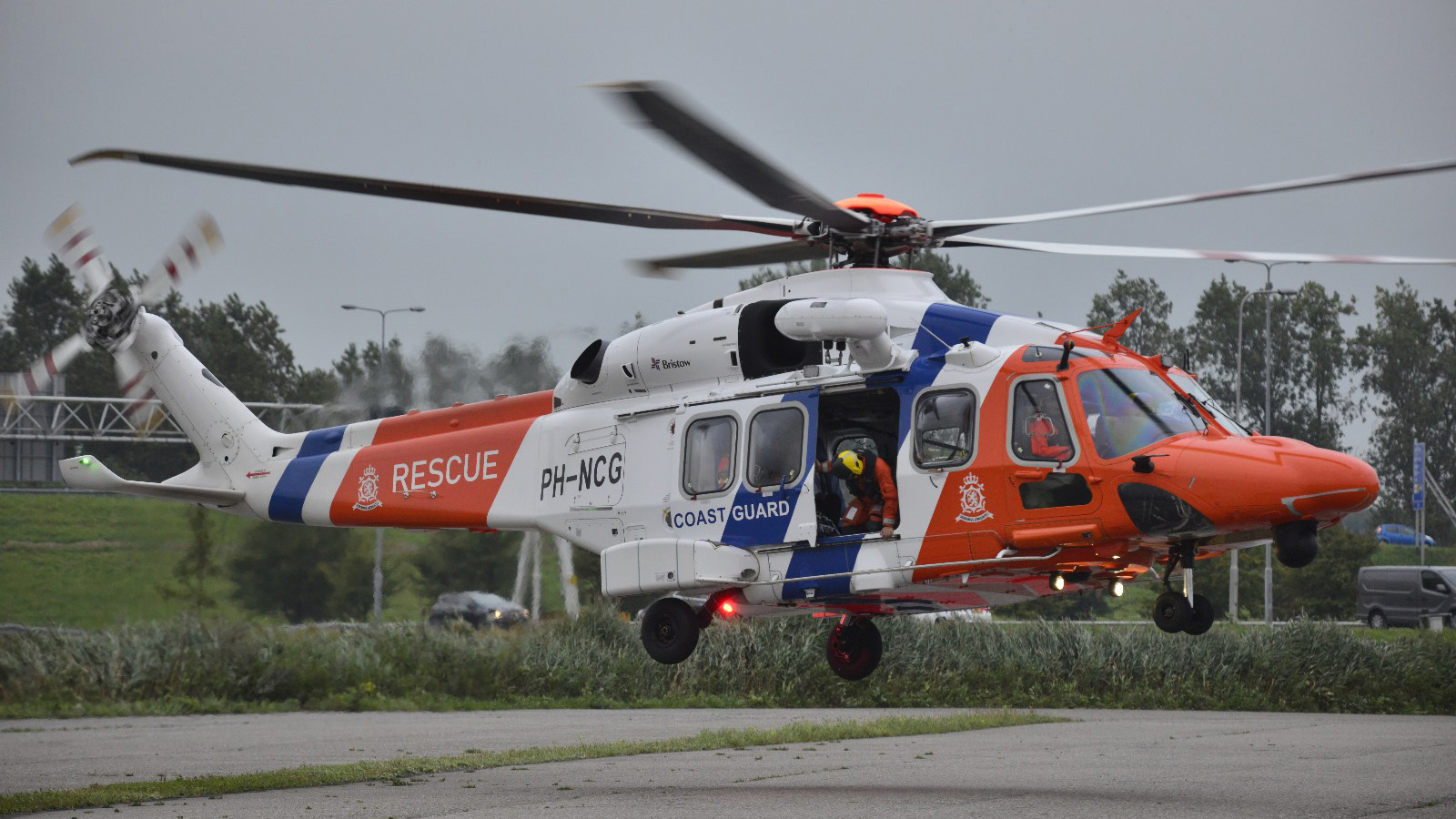 Kustwachthelikopter tijdens reddingsoperatie, net boven de grond zwevend.