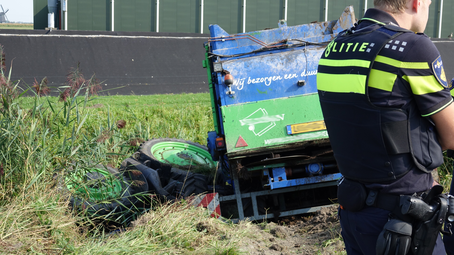 Politieagent bij een gekantelde landbouwvoertuig in een berm.