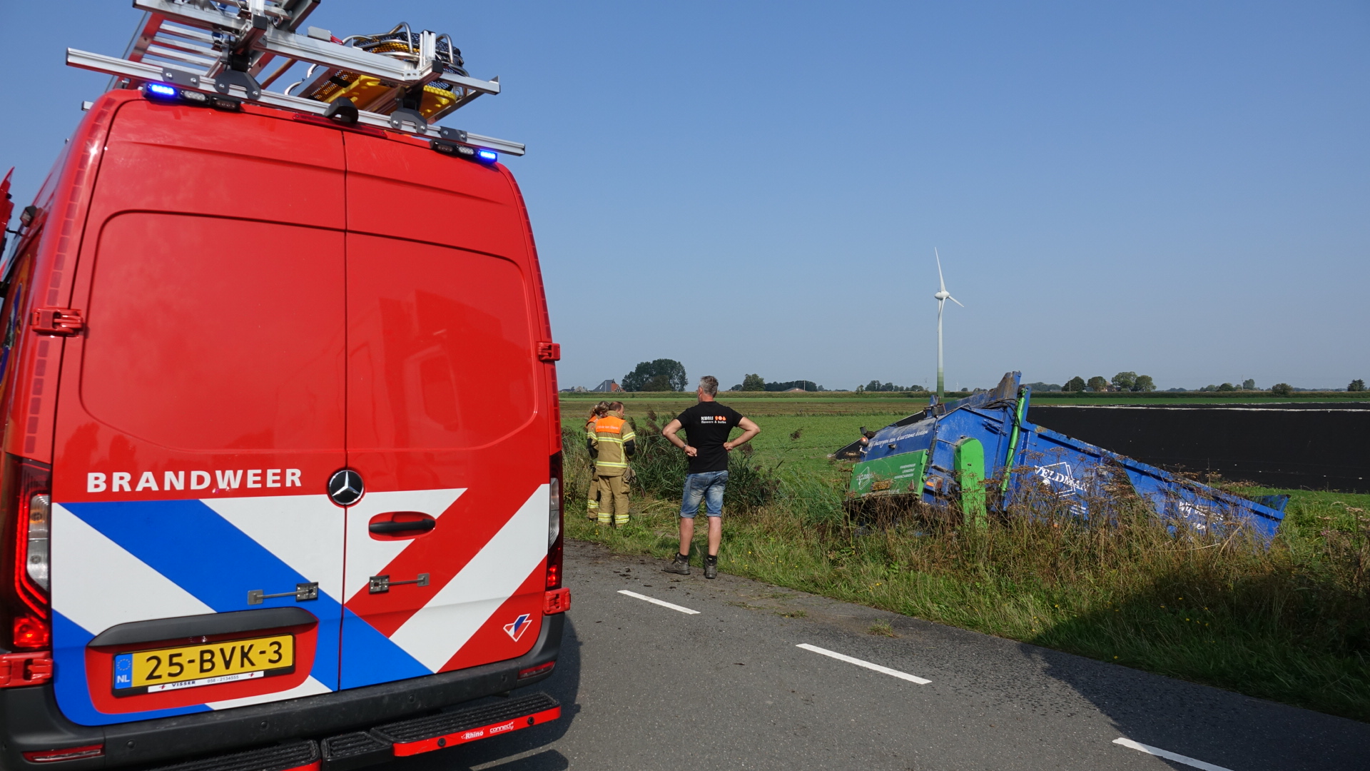 Brandweerauto en personeel op de plaats van een ongeval met een omgevallen trailer in een weiland.