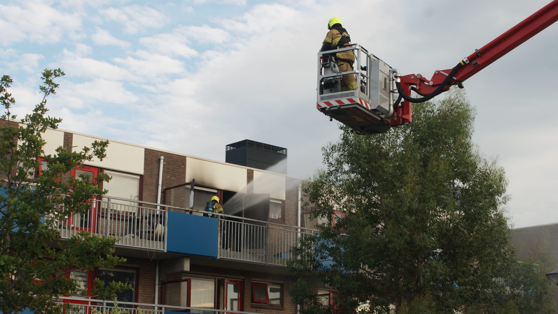 Brandweerlieden blussen brand in een appartement op de tweede verdieping van een gebouw.