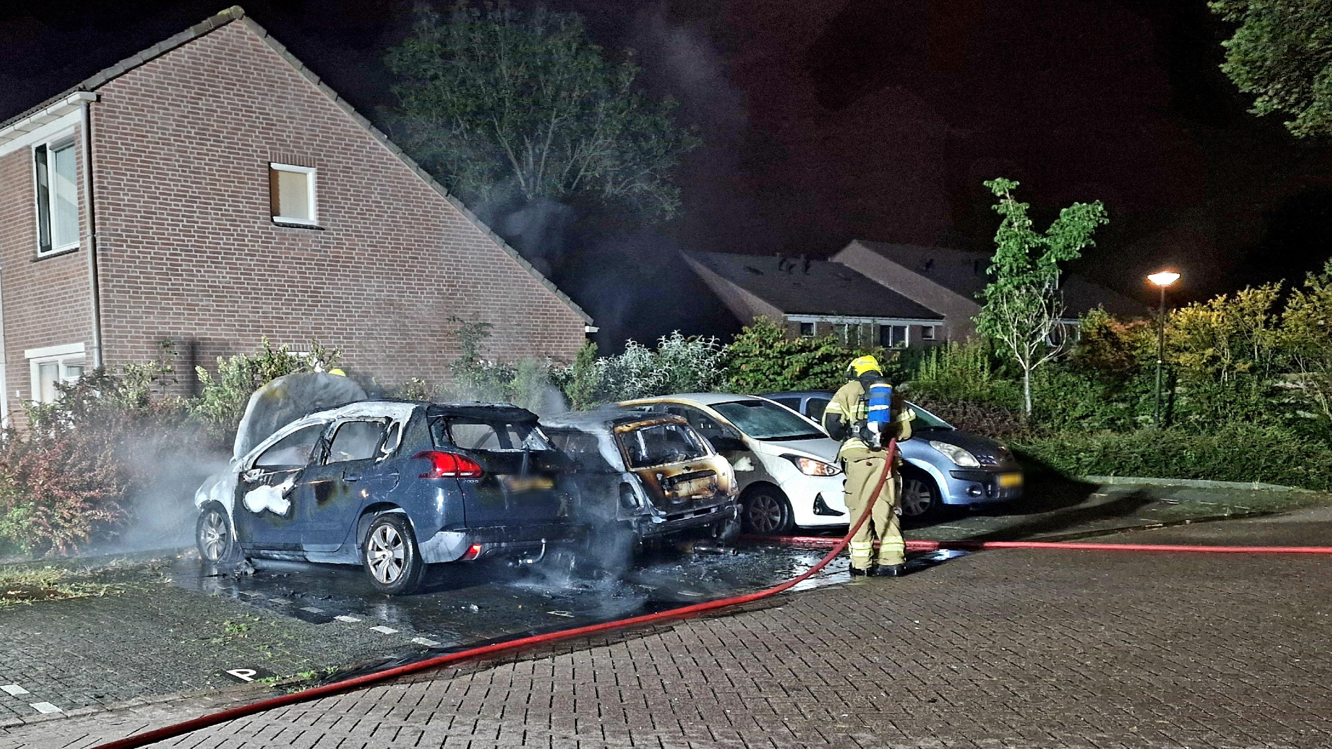 Brandweerman blust paar auto's die 's nachts in brand staan naast huis.